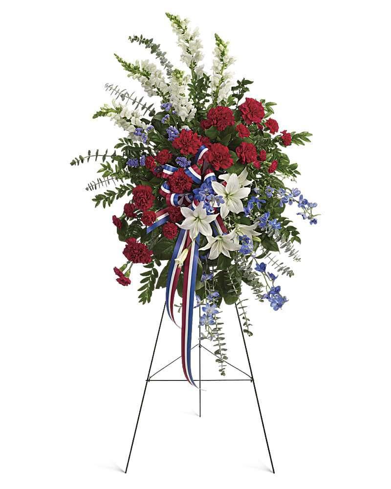 Sacred Duty Memorial Spray - The Sacred Duty Memorial Spray from DGM Flowers is a stunning tribute to honor the memory of a loved one. This patriotic funeral sprays sparkles like an Independence Day fireworks display, a striking red, white and blue Sacred Duty spray stands tall proud and patriotic. Bearing the colors of our nation's flag, it's a grand and fitting tribute to members of the military and American heroes.&nbsp; &nbsp;  Adorned with yards of multicolored patriotic ribbon, this easel-mounted standing spray features flowers such as red carnations, white asiatic lilies and snapdragons, and blue delphinium, along with an assortment of greens. Orientation: One-Sided Size: 42&quot; H 27&quot; W