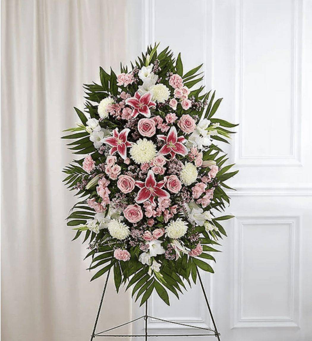 Pink &amp; White Funeral Standing Spray - The warmth and kindness they showed will live on forever, and sometimes this sentiment is best captured through flowers. Our classic standing spray arrangement is elegantly crafted with soothing pink and white blooms for a lush, full presentation, creating a truly memorable tribute to someone so loved. Order the Pink &amp; White Funeral Standing Spray for a heartfelt expression of love and support during a difficult time. Ideal for those searching for pink and white funeral flowers. &nbsp;  One-sided standing spray arrangement with pink roses, spray roses, Stargazer lilies, Peruvian lilies (alstroemeria), carnations and waxflower, white gladiola and football mums; accented with assorted greenery Ultra Premium arrangement measures approximately 60&quot;H x 40&quot;W without stand Premium arrangement measures approximately 56&quot;H x 38&quot;W without stand Deluxe arrangement measures approximately 46&quot;H x 34&quot;W without stand Standard arrangement measures approximately 42&quot;H x 30&quot;W without stand Arrives on an easel Appropriate for the funeral home or gravesite We hand-design every arrangement, so colors and varieties may vary due to local availability