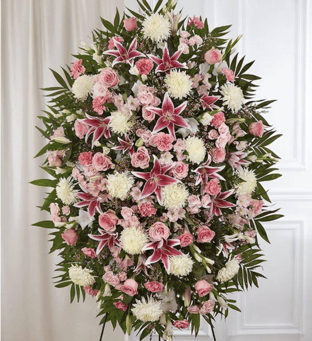 Pink &amp; White Funeral Standing Spray PREMIUM - The warmth and kindness they showed will live on forever, and sometimes this sentiment is best captured through flowers. Our classic standing spray arrangement is elegantly crafted with soothing pink and white blooms for a lush, full presentation, creating a truly memorable tribute to someone so loved. Order the Pink &amp; White Funeral Standing Spray for a heartfelt expression of love and support during a difficult time. Ideal for those searching for pink and white funeral flowers. &nbsp;  One-sided standing spray arrangement with pink roses, spray roses, Stargazer lilies, Peruvian lilies (alstroemeria), carnations and waxflower, white gladiola and football mums; accented with assorted greenery Ultra Premium arrangement measures approximately 60&quot;H x 40&quot;W without stand Premium arrangement measures approximately 56&quot;H x 38&quot;W without stand Deluxe arrangement measures approximately 46&quot;H x 34&quot;W without stand Standard arrangement measures approximately 42&quot;H x 30&quot;W without stand Arrives on an easel Appropriate for the funeral home or gravesite We hand-design every arrangement, so colors and varieties may vary due to local availability