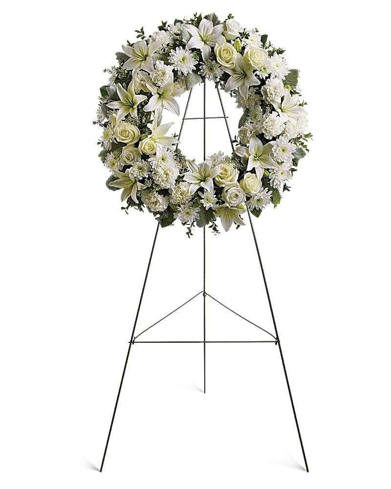 Serenity White Wreath - The Serenity White Wreath by DGM Flowers | Fort Lauderdale Florist is a stunning addition to any funeral or memorial service. This fresh cut flower wreath is elegantly designed with white blooms symbolizing peace and serenity. Fragrant and ethereal white blossoms set among a ring of soothing greens form a classic Serenity wreath certain to evoke the pure heart and gentle spirit of a loved one - and offer consolation during a funeral or wake. The crisp white colors and delicate design make this White Funeral Wreath a perfect tribute to honor a loved one. Trust DGM Flowers for high-quality floral arrangements that convey sympathy and comfort during difficult times. &nbsp;  Delivered on an easel, a standing wreath comprising fresh flowers such as white roses, asiatic lilies, carnations and chrysanthemums, as well as greens including salal, oregonia and dusty miller. Orientation: One-Sided Size: 22&quot; H. 22&quot; W