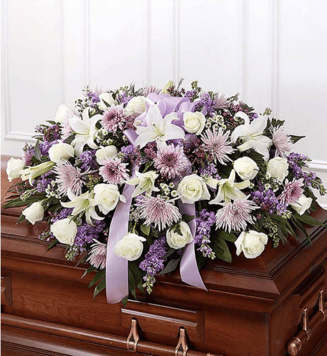 Lavender &amp; White Mixed Half Casket Cover - When we lose someone dear to us, we want to respond with a fitting gesture of respect and admiration. Our half casket cover, crafted with care and artistry by our expert florists with lavender cremones, mums, white roses, and accented with a lavender satin ribbon, is an unforgettable way to commemorate a lifetime of loving devotion. Make your final tribute memorable with the stunning Lavender Casket flowers.  &nbsp;  Half casket cover arrangement of white roses, hybrid lilies and monte casino, lavender cremones, spider mums and stock, purple waxflower and fresh greenery; accented with a lavender satin ribbon Arrangement measures approximately 16&quot;H x 38&quot;L x 26&quot;D Traditionally sent by the immediate family to the funeral home We use only the freshest flowers available, so colors and varieties may vary