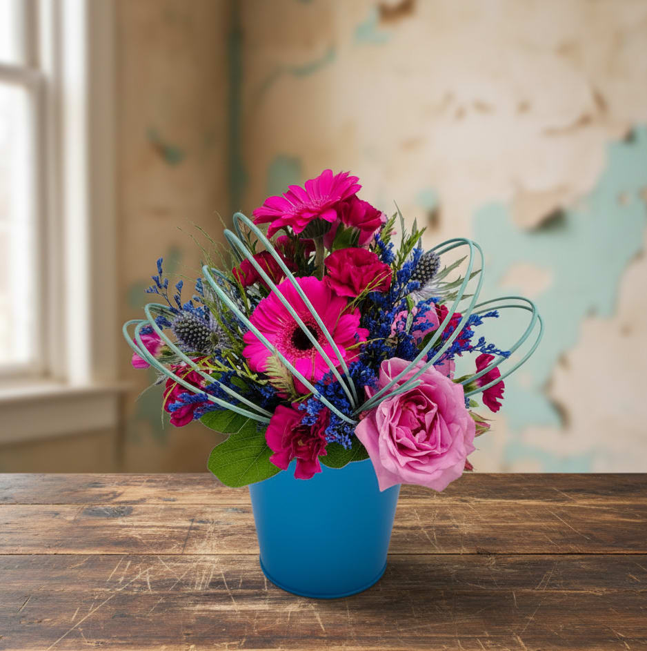 Blueberry Bliss - Blueberry Bliss  Looking for the perfect flower gift in Olympia, WA? Blueberry Bliss is a cheerful and vibrant floral arrangement designed to brighten any day, whether you're celebrating a birthday, Mother’s Day, or sending a thoughtful get well soon gesture.  This fun design features a playful mix of moody purples, rich blues, and magentas. You'll find mini carnations, lavender roses, and bold magenta gerbera daisies artfully arranged and wrapped in midollino sticks for a fun and modern twist. The flowers are presented in a vibrant 4-inch blue container that adds an extra pop of color and charm to any space.  Compact in size, Blueberry Bliss is perfect for a desk at work, a bedside table, or a hospital room—anywhere that needs a splash of beauty and color.  We offer same-day flower delivery in Olympia, WA, and serve the surrounding areas, including Tumwater, WA, Lacey, WA, and more. Whether you're sending flowers to a loved one at home, in the office, or at a local hospital, Specialty Floral Design is here to help you deliver joy with flowers.