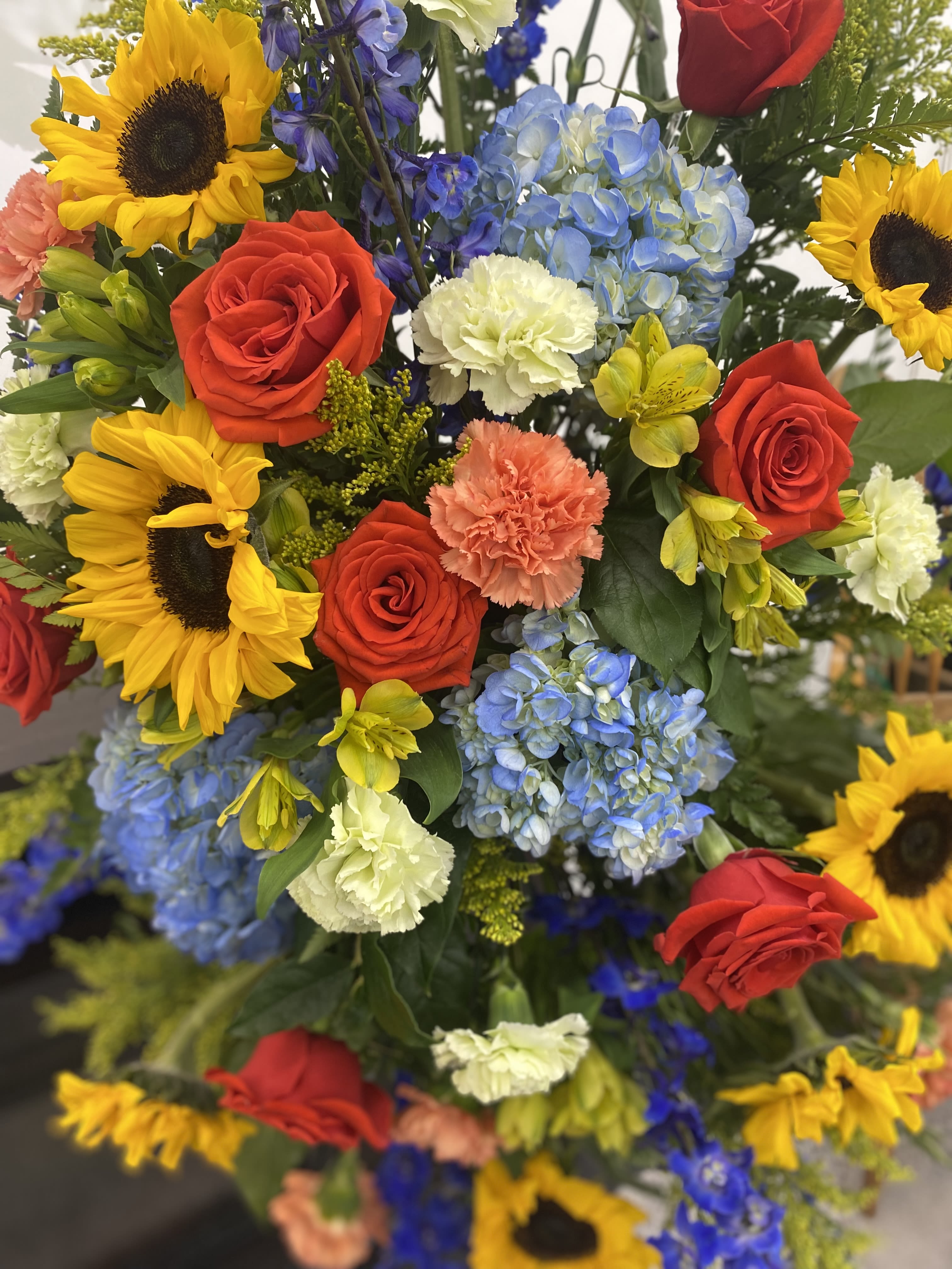Rays of Life - This breath taking standing spray is bright and full of love. These colors are perfect for remembering someones radiant life. A mix of roses, sunflowers, delphinium, solidago, hydrangeas, carnations, and alstroemeria fit perfectly together and are sure to make a statement. 