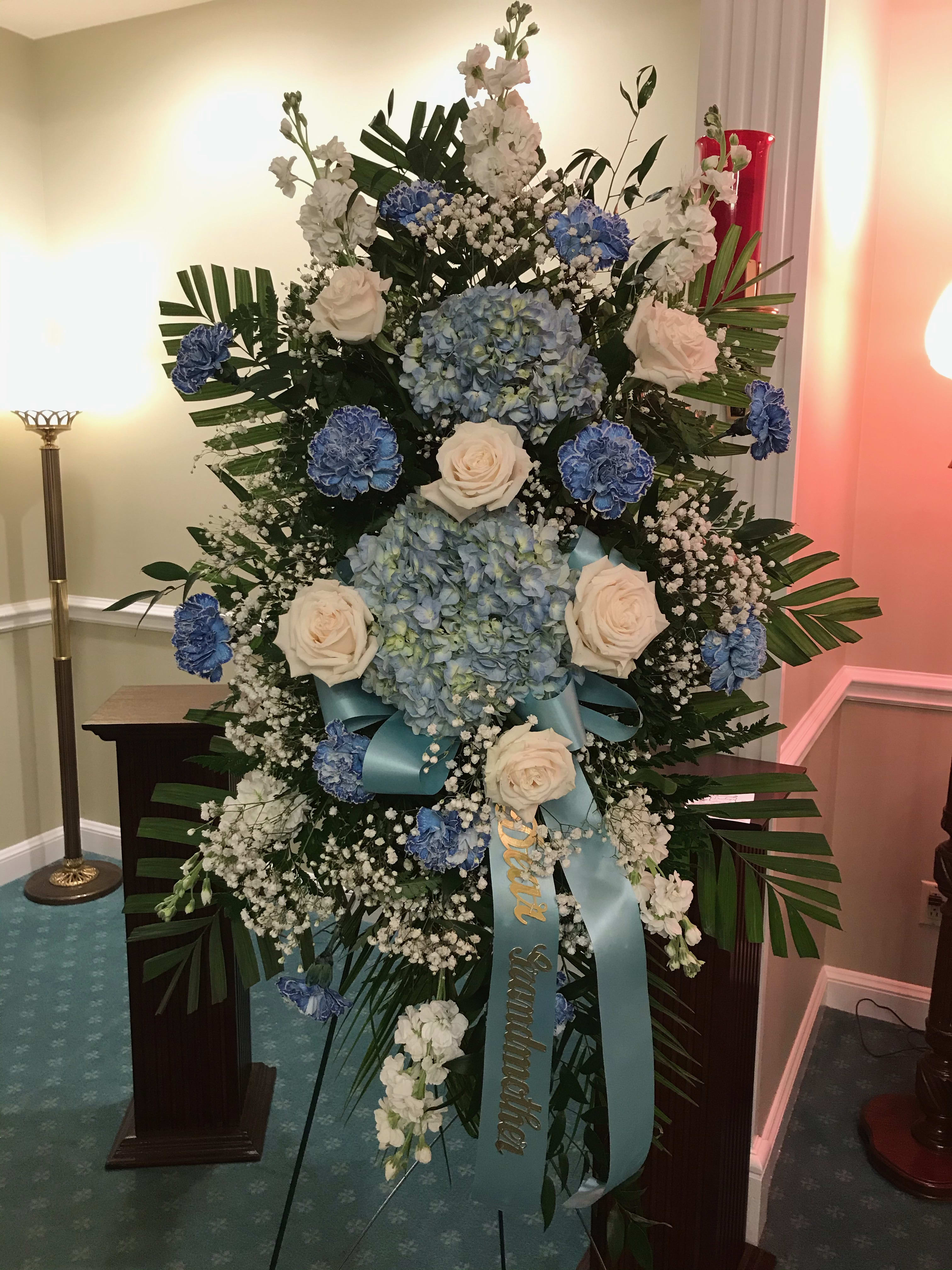 Blue and White Easel - A large standing easel arrangement of Blue Hydrangeas, blue carnations, white roses, white stock, baby's breath and greenery.  This arrangement stands approximately 6'.