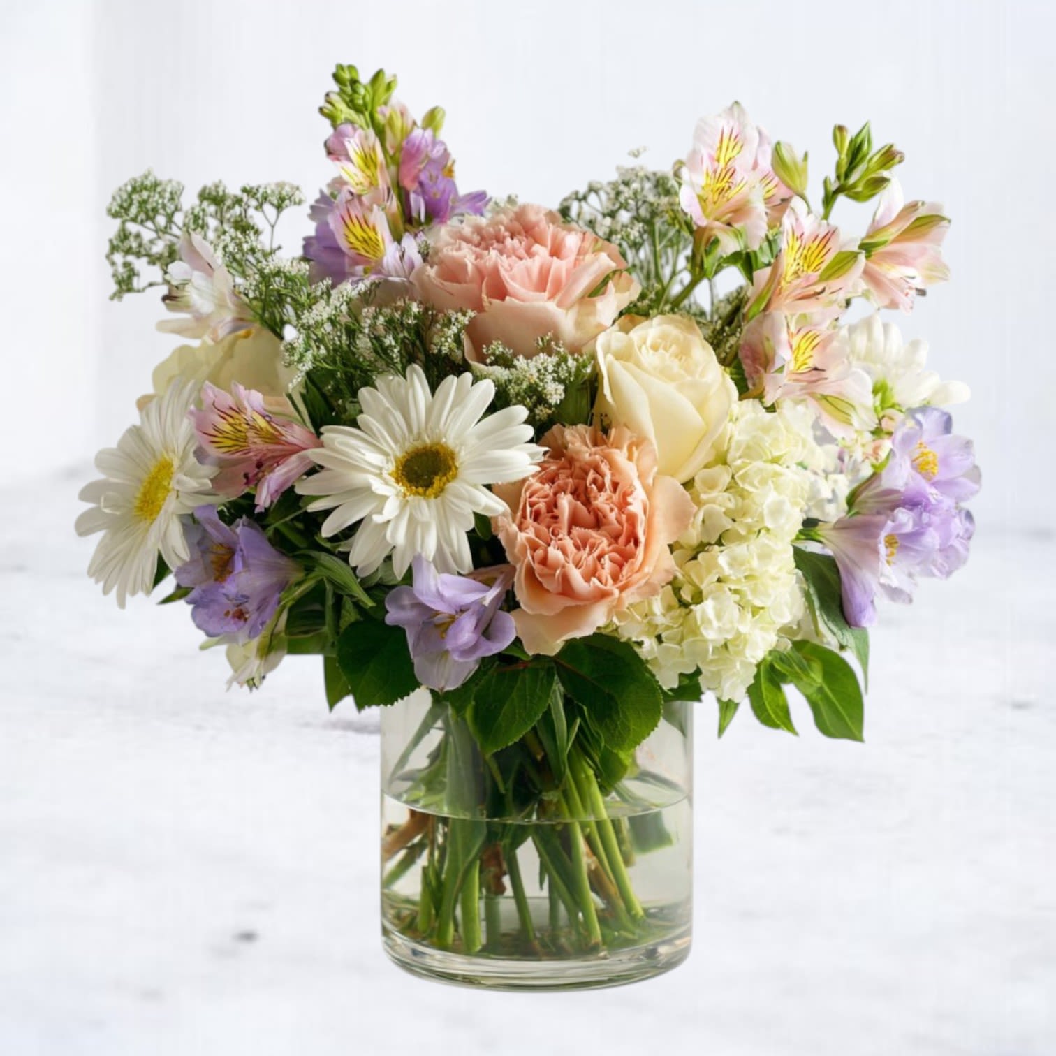 Sunny Cheer Bouquet - Brighten someone’s day with the Sunny Cheer Bouquet, a joyful mix of fresh mini gerbera daisies, white roses, lavender blooms, and creamy hydrangeas. Designed in a clear glass vase, this bouquet blends soft pastels with playful textures for a look that’s both elegant and uplifting. Perfect for birthdays, get-well wishes, thank-yous, or just-because moments, it’s a timeless choice for everyday gifting that delivers smiles with every petal.  Available for same-day delivery in Magnolia, The Woodlands, Spring, Montgomery, and surrounding areas.