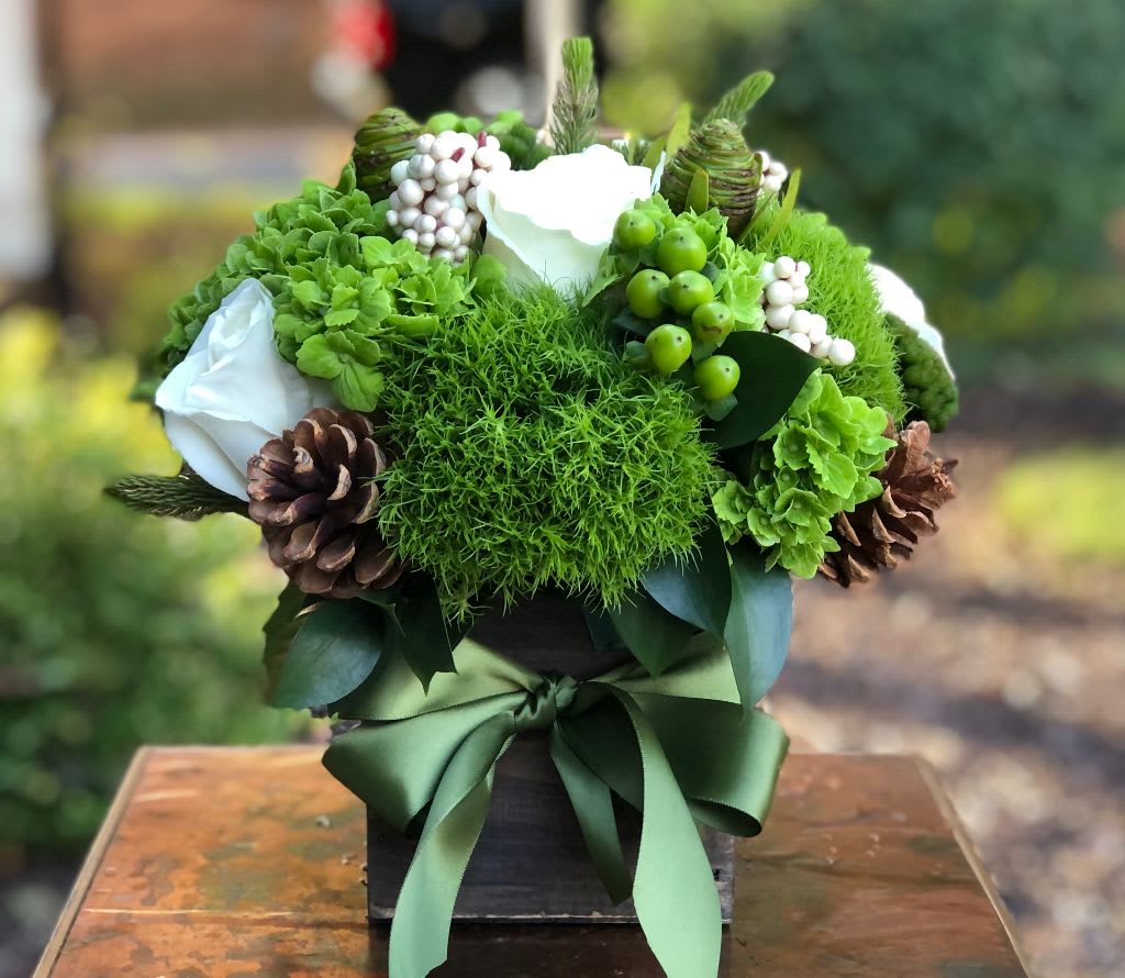 The Greenville  - The Greenville – Elegant Green &amp; White Floral Arrangement by Petals in Wilmington, Delaware   Inspired by the natural beauty of Delaware’s Brandywine Valley, The Greenville is a refined and timeless floral arrangement handcrafted by Petals, your trusted local Wilmington, Delaware florist. This elegant design features lush green hydrangea, textured green trichilium, fresh green hypericum berries, and classic white roses, accented with white blooms and rustic pine cones for a soft, seasonal touch. Arranged in a natural wooden square box and finished with a green satin ribbon, The Greenville perfectly balances modern elegance and organic charm. Ideal for winter celebrations, holiday centerpieces, or everyday sophistication, this versatile design brings a touch of Wilmington’s serene landscape indoors.Handcrafted with care by Petals’ floral designers in Wilmington, DE  Available for same-day flower delivery in Wilmington, Delaware, and surrounding areas including Greenville, Hockessin, Newark, Kennett Square and The Brandywine Valley. Every arrangement is designed and delivered fresh from Petals, Wilmington’s premier local florist for over 20 years. 