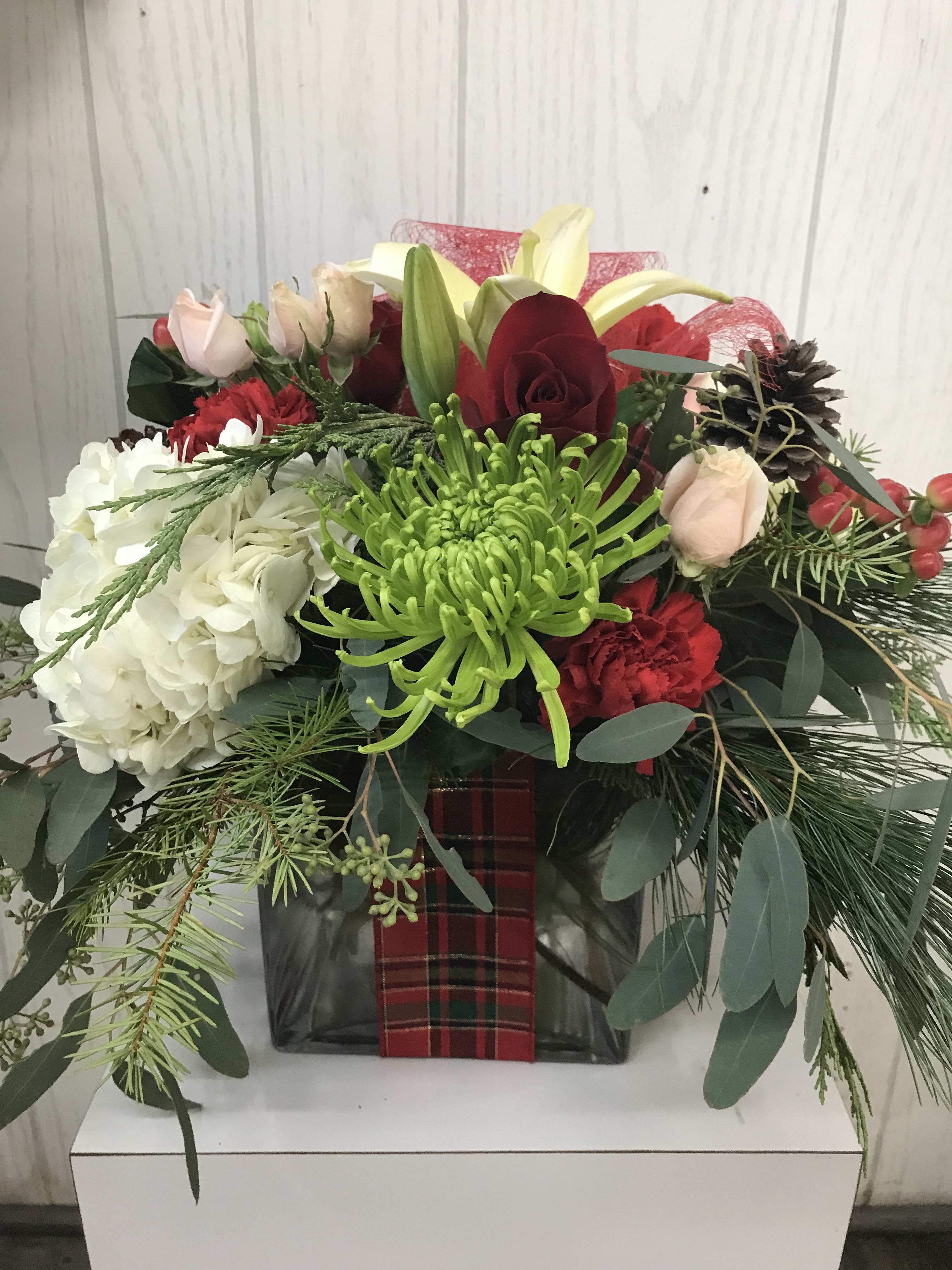 Modern Holiday Package Centerpiece - A floral twist on a holiday package, this arrangement is filled with beautiful holiday flowers. Designed in a large clear glass cube. It is accented with a festive holiday ribbon. This package is sure to make a statement! Approx. 13 inches H x 14 inches W. Deluxe &amp; premium include more flowers. ***FLOWER SUBSTITUTIONS/DESIGNER’S CHOICE*** is required due to limited product offerings. The flowers may be substituted, but the beauty and price value will be maintained. Thank you for your understanding!   