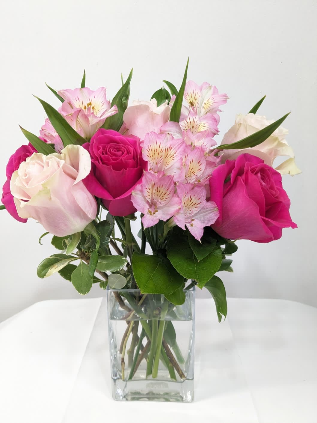 Pink Bloom - This cute and cheerful bouquet includes light pink roses, hot pink roses and pink alstroemeria. Delivered in a 6&quot;H square glass vase.