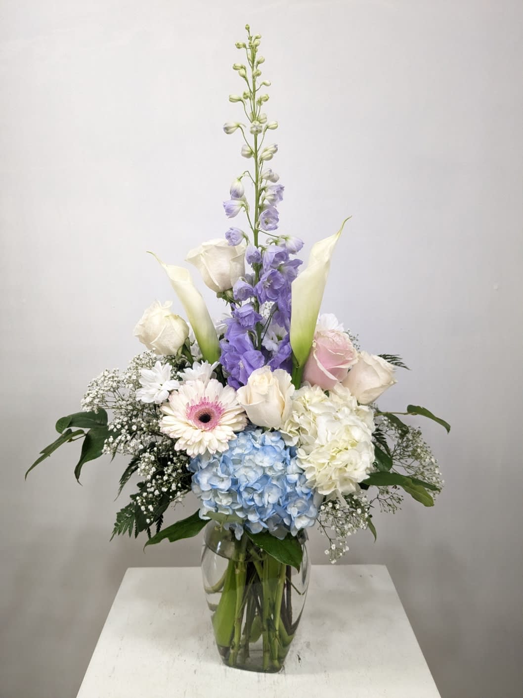 Elegance Dream - This tall sculptural bouquet of soft purple/blue delphinium, Calla lily and two soft color hydrangea adds artistic elegance to any event! Delivered in a clear jug vase.