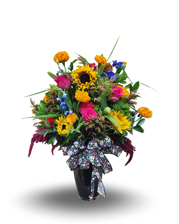Colorful Remembrance - Celebrate life and love with this radiant all-around floral arrangement bursting with color and texture. Featuring bold sunflowers, vivid pink roses, marigolds, blue delphinium, and lush greenery, this piece brings warmth and brightness to any space. Designed in a sleek black vase and finished with a festive printed bow, it’s perfect for honoring joyful memories or adding vibrant beauty to any occasion.  Approximate size: 26”H x 17”W x 17”D.