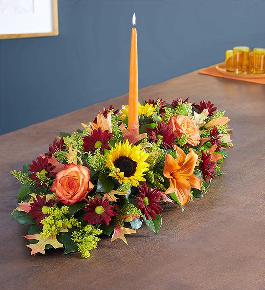 Autumn Centerpiece- CANDLE COLOR MAY VARY - A traditional look for your Thanksgiving table, available in Standard and Large sizes. Sunflowers, chrysanthemums, roses, lilies, fall leaves and fillers in reds, oranges and yellows make up this classic Thanksgiving Centerpiece. Not a fan of Candles? No worries! Say &quot;NO CANDLE(S)&quot; in the special instructions and we will just make them more lush with with florals