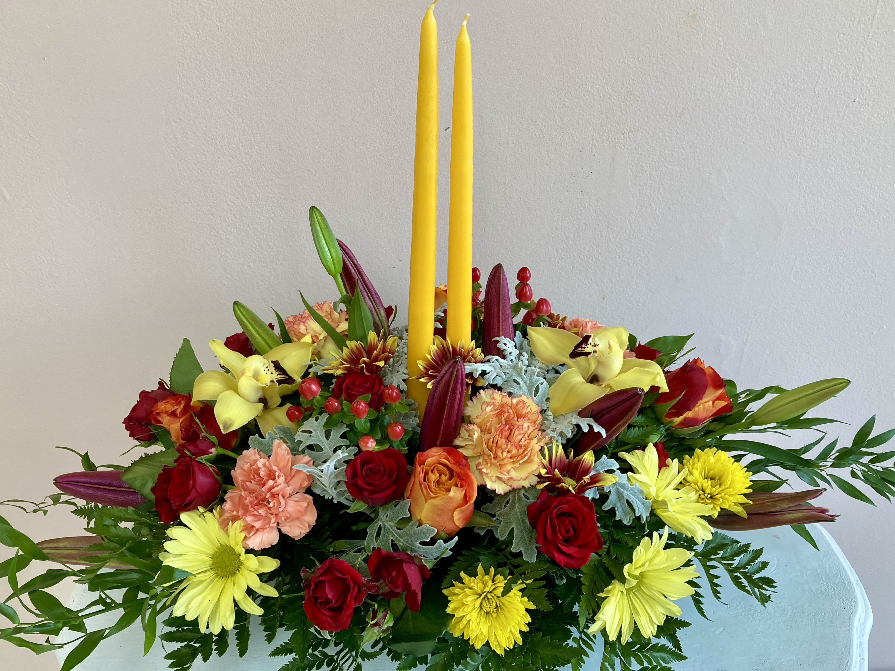 TG 4 - Thanksgiving centerpiece featuring an assortment of fall flowers arranged in a floral foam container.  * Candle color and florals may vary based on availability.