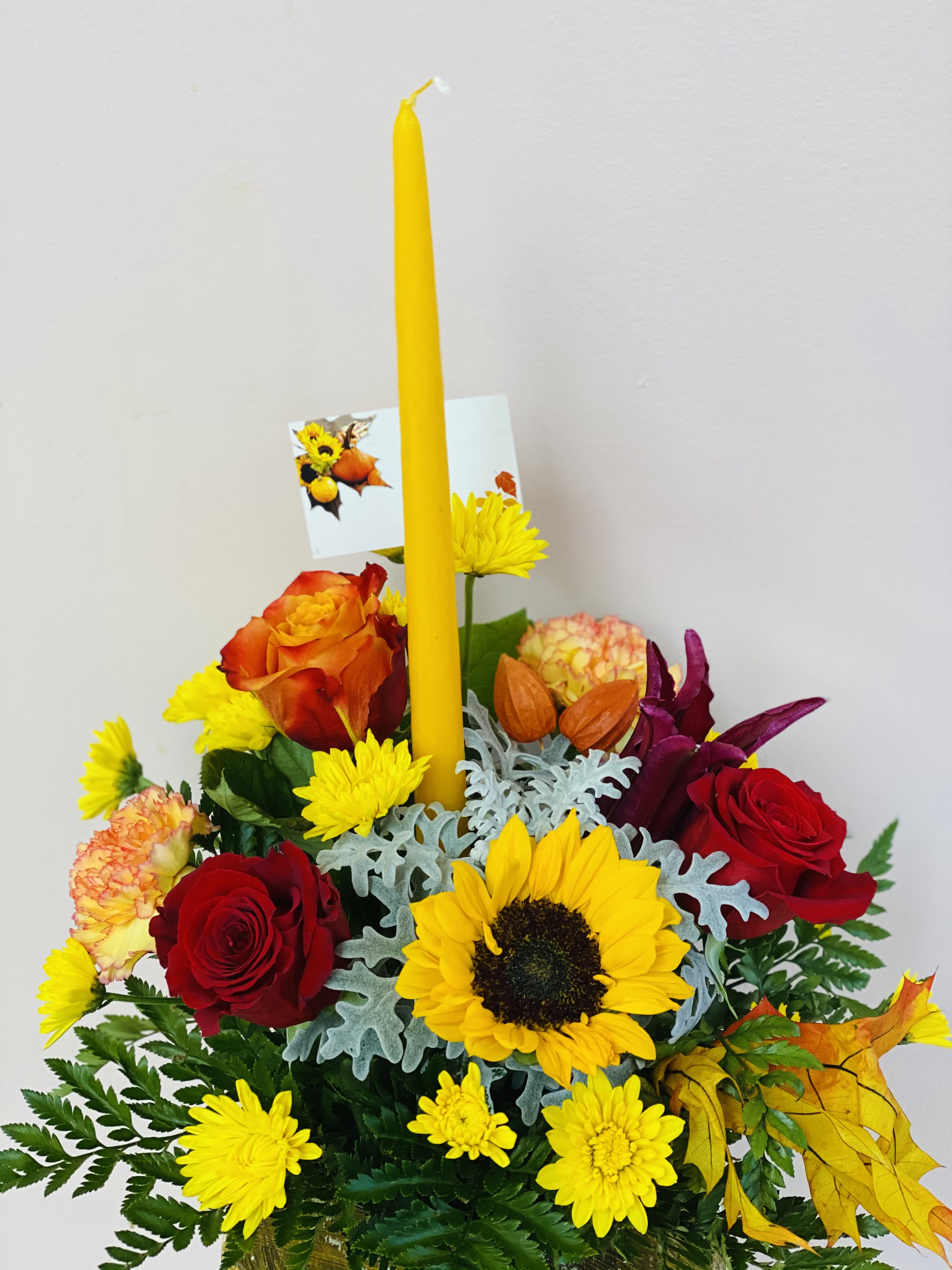 TG 5 - Thanksgiving centerpiece featuring an assortment of fall flowers arranged in a floral foam container.  * Candle color and florals may vary based on availability.