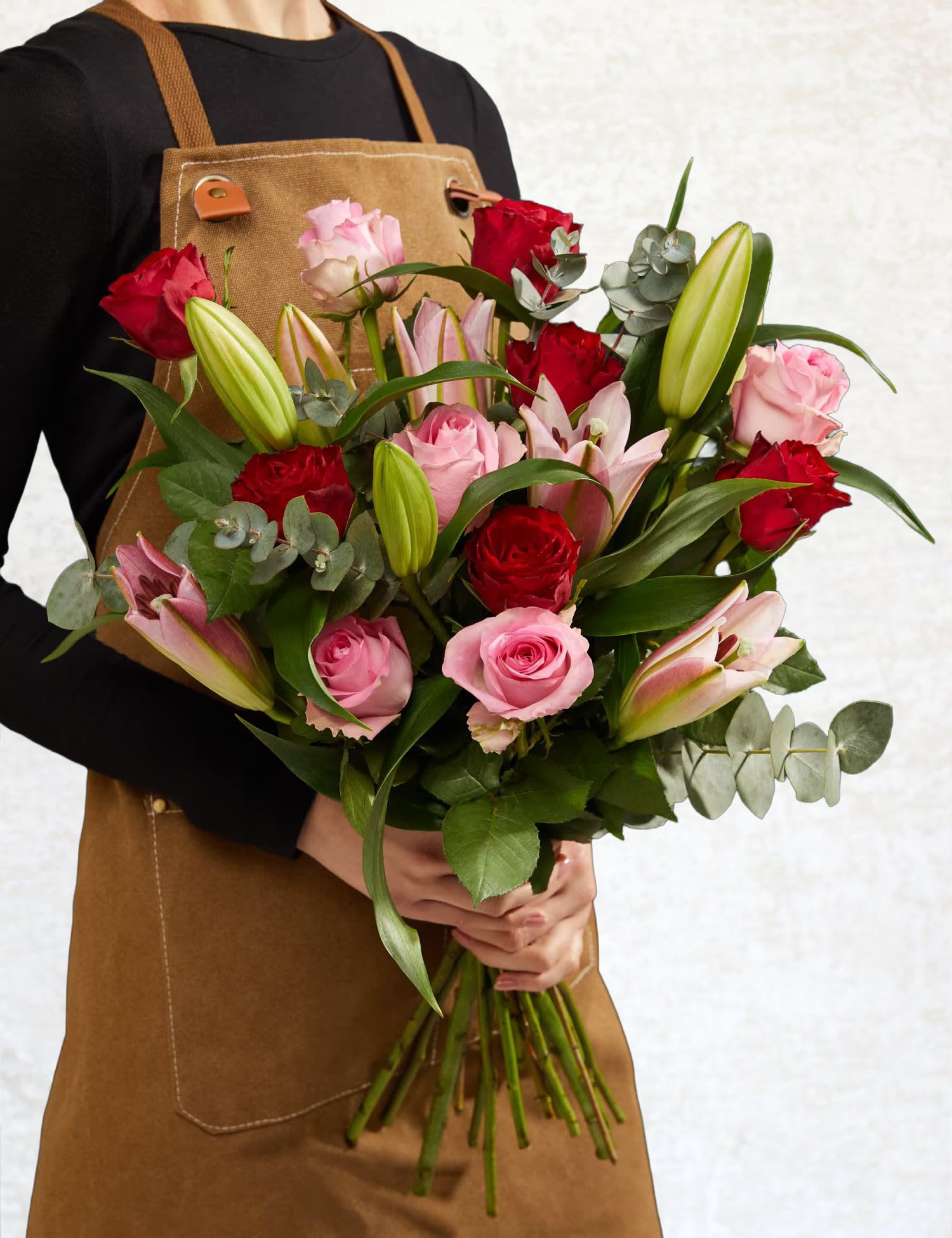 Scarlet Embrace Bouquet - Indulge in the timeless elegance of the Scarlet Embrace Bouquet, a breathtaking arrangement that captures the essence of romance and grace. Featuring velvety red roses, soft pink roses, and exquisite pink premium lilies, all complemented by fresh eucalyptus, this bouquet is a stunning display of love and beauty. Whether you're celebrating an anniversary, expressing admiration, or simply adding a touch of luxury to your space, this captivating arrangement is the perfect choice to make any moment unforgettable.  What's included?  Red Roses, Pink Roses, Pink Premium Lilies, and Eucalyptus.