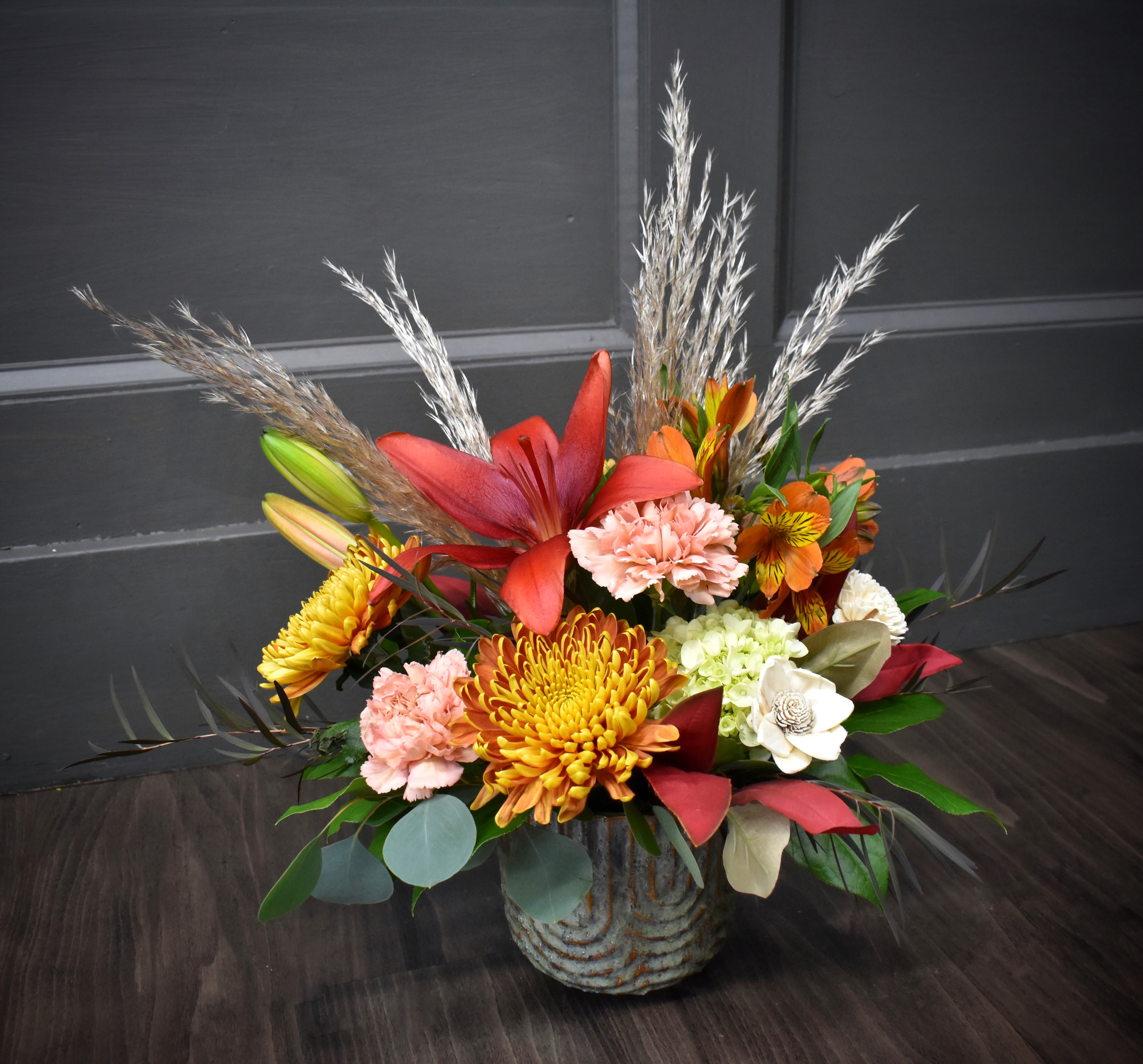 Rustic Radiance - Beautiful lilies, fluffy mums and a wooden flower designed in a pottery vase with an assortment of lush foliage.
