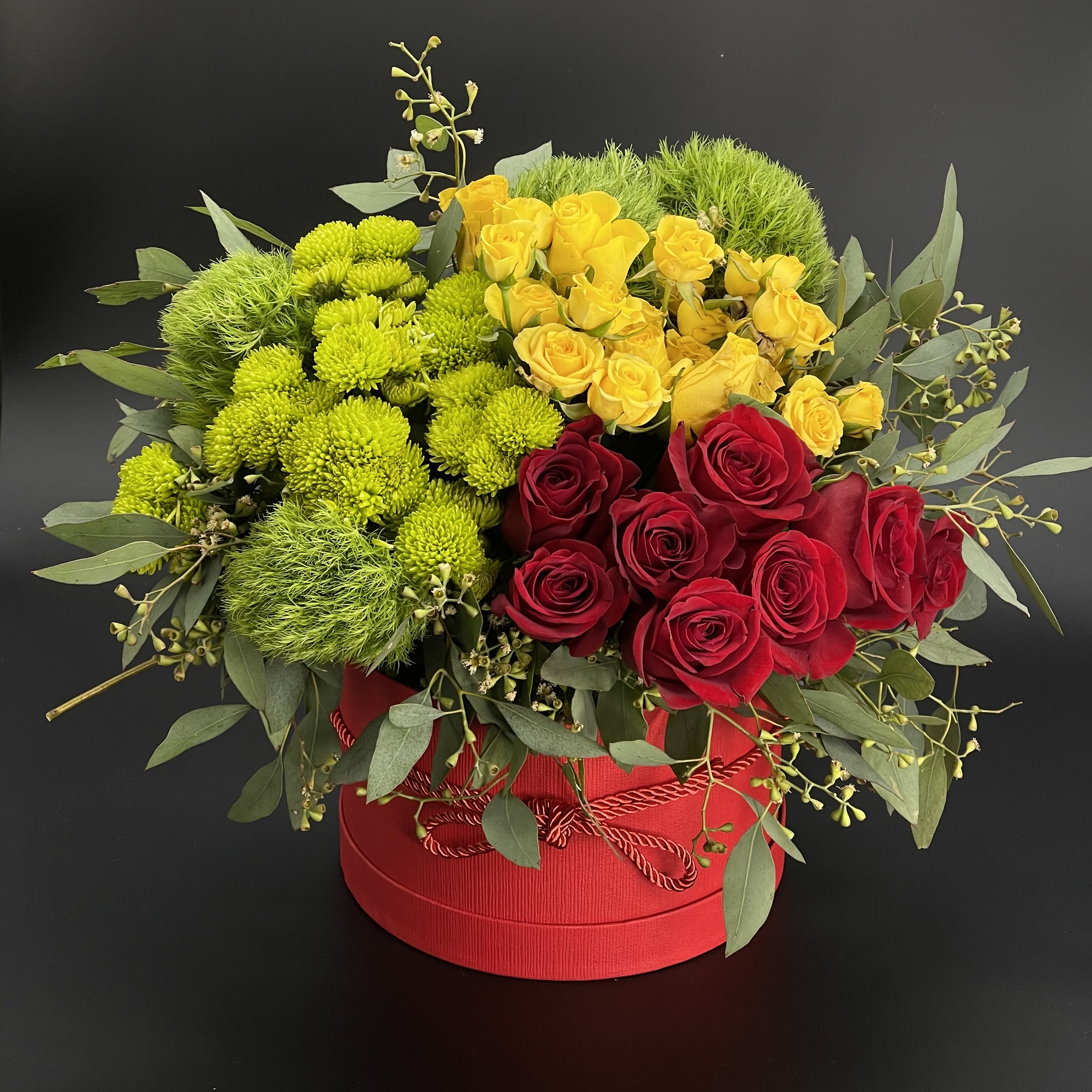  Fiery Red - A Red Round Box with Red Roses, Yellow spray Roses, Green Pom poms with lush Greenery.