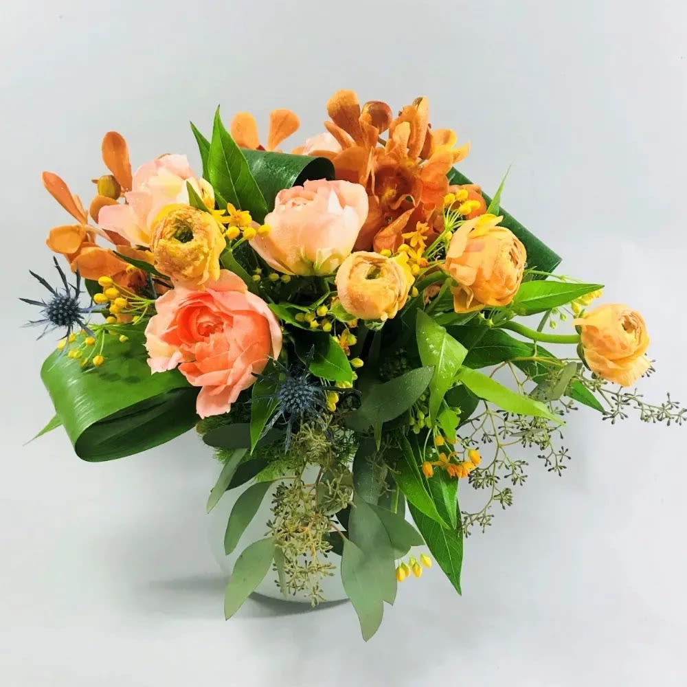 Topaz - A low compact arrangement of all seasons gathering. Comprised of green dianthus, thistle, seeded eucalyptus, orange ranunculus, deep orange mokara orchids, and pink garden roses.