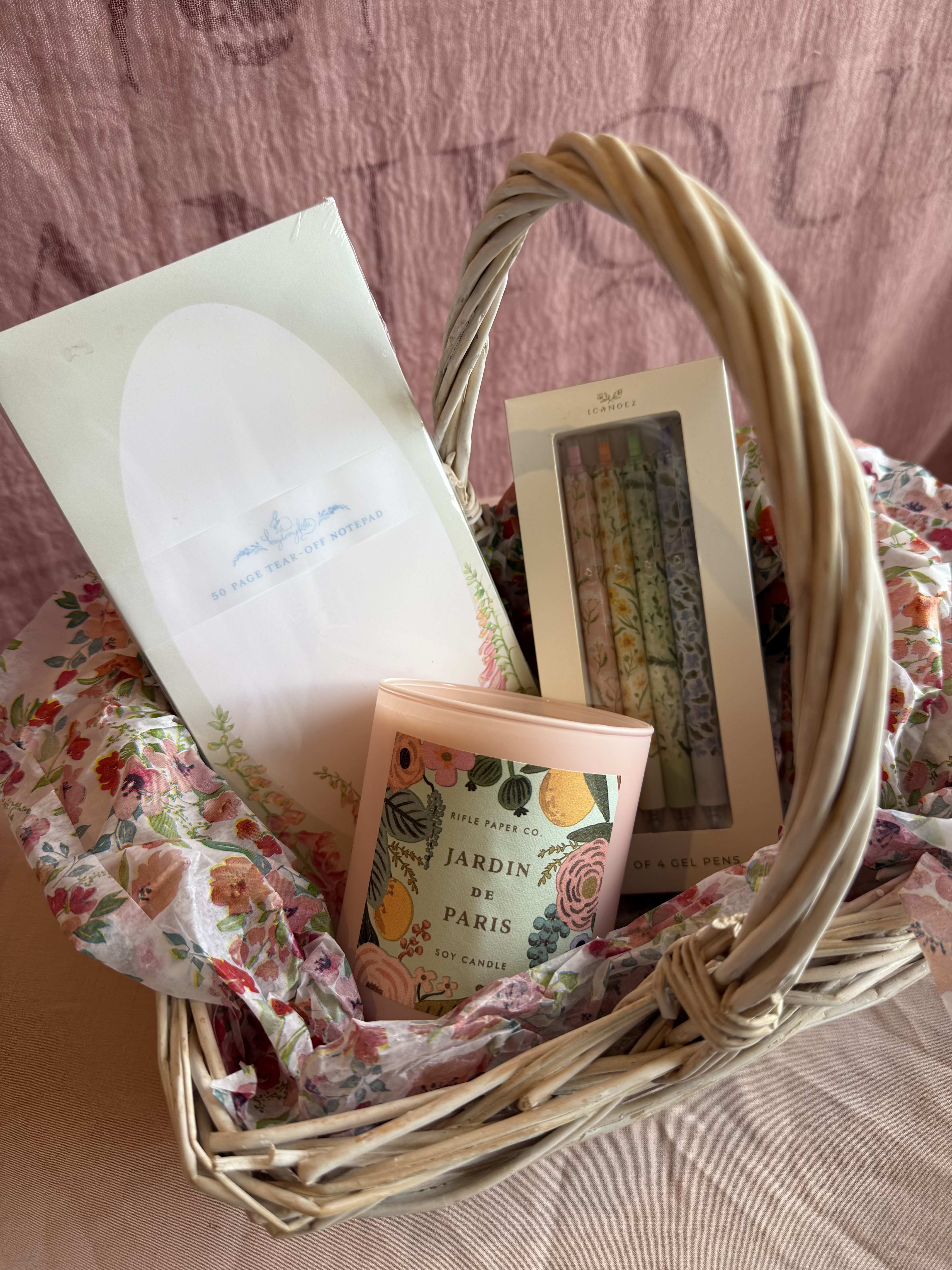 The Cozy Desk Gift Basket  - Turn any workspace into a warm little haven with this thoughtfully crafted gift basket. Perfect for a cozy afternoon, creative minds, or anyone who loves to make their desk feel like home.   Gift basket includes:  1 Bayberry Kate, Foxglove 50 page notepad 1 1canoe2, Roadside Blooms 4 gel pen set 1 Rifle Paper Co. - Jardin De Paris Soy Candle  (9.5oz - Peony,  white tea, gardenia, sandalwood)  