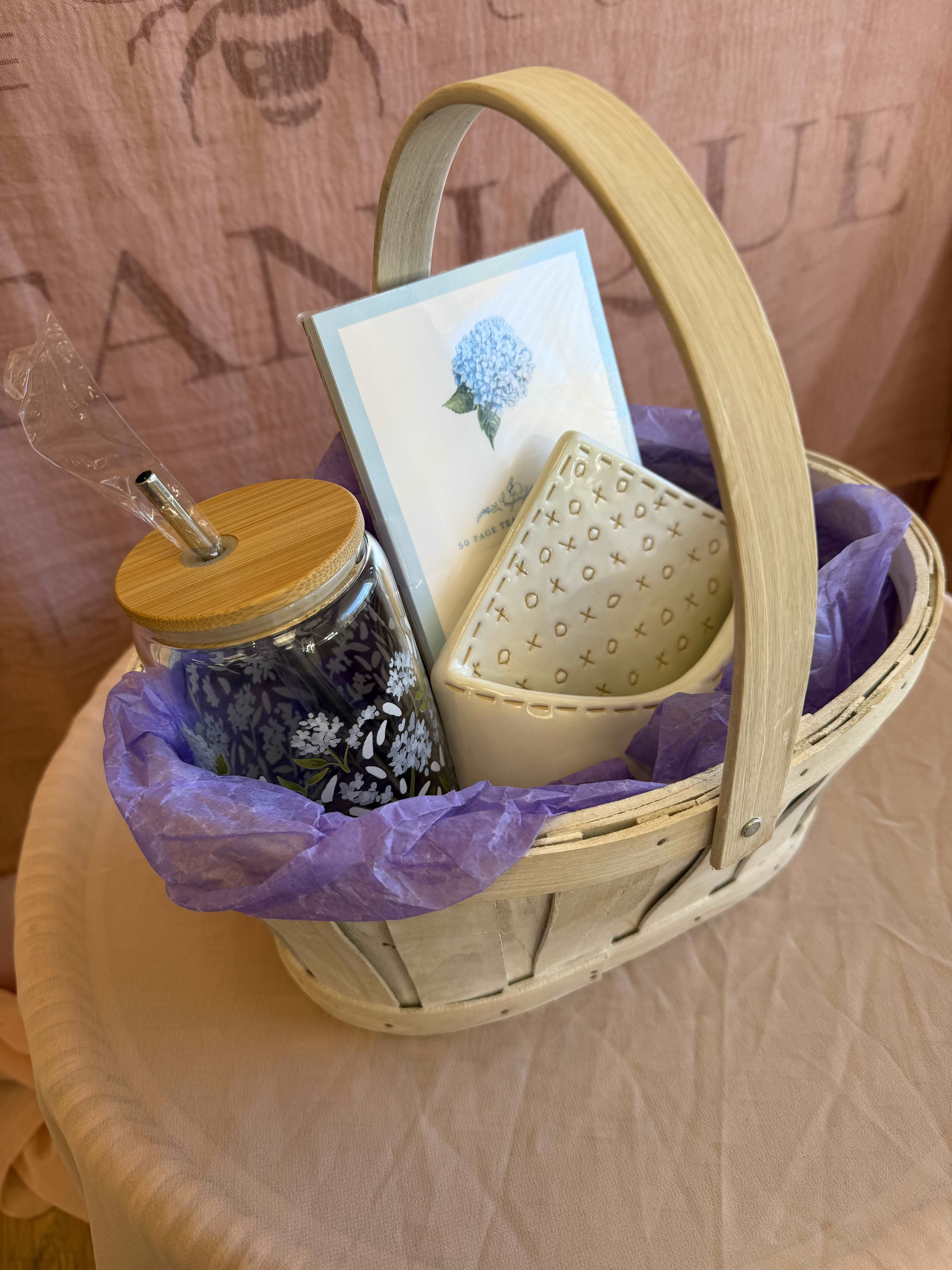 The Petite Hydrangea Gift Basket - Bring the charm of Cape Cod's favorite bloom to your desk or kitchen with our hydrangea gift set. This beautifully coordinated collection includes, a petite envelope bud vase for fresh stems, a glass drinking cup adorned with delicate hydrangea detail (complete with a reusable metal straw!) and a matching hydrangea notepad for your sweet thoughts and to-do-lists. It's a petite burst of coastal calm - wrapped up and ready to gift!  Gift Basket Includes:  1 With love ceramic envelope bud vase  1 1canoe2 Hydrangea glass, metal straw  1 x Bayberry Kate - Hydrangea notepad 