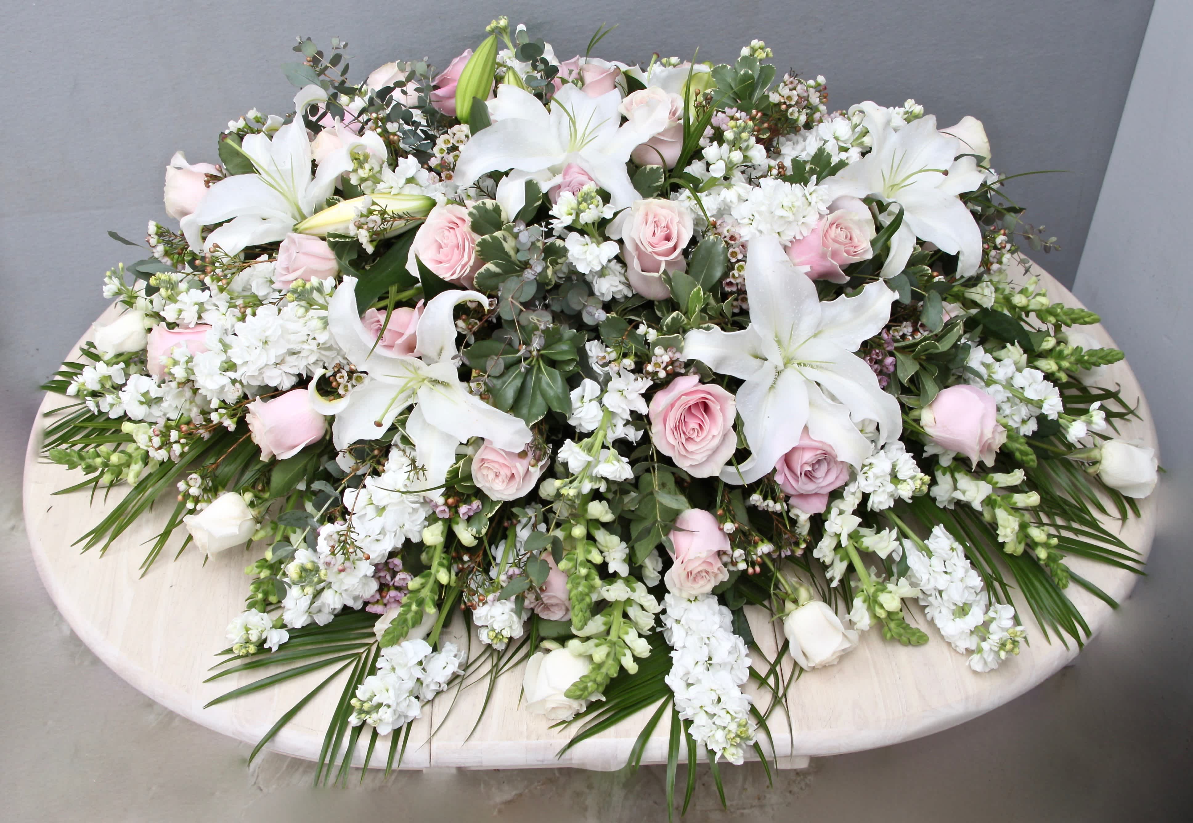 Pink and White Casket  - This casket arrangement is made with pink and white roses, stargazer lilies, and fragrant seasonal greens.     Standard size is half casket, deluxe is 3/4 and premium is full casket.