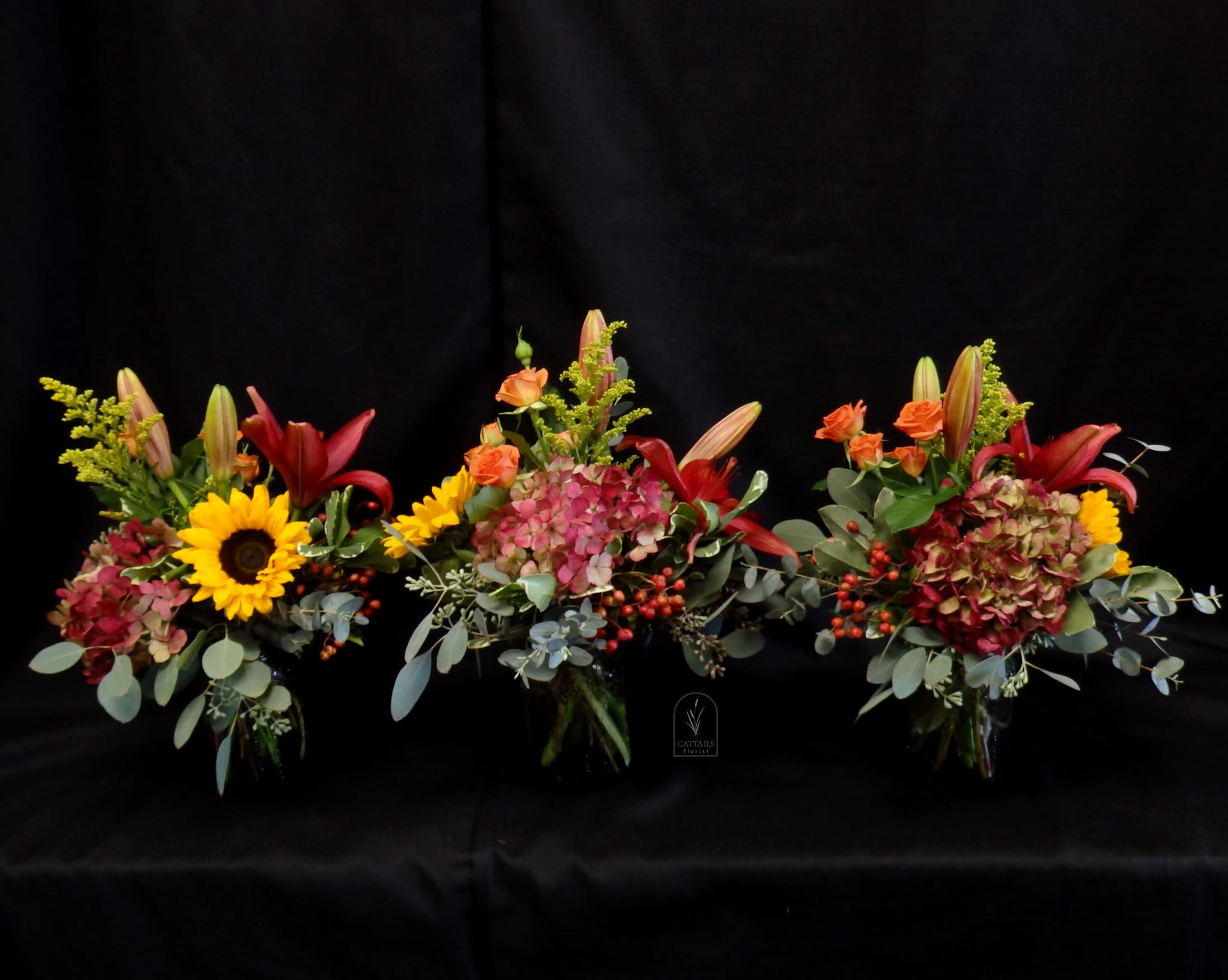 Autumn Trio - A festive centerpiece that works great for a long table that is full of food. 3 mini vases with fall hydrangeas, lilies, sunflowers and spray roses to give that feeling of autumn!  