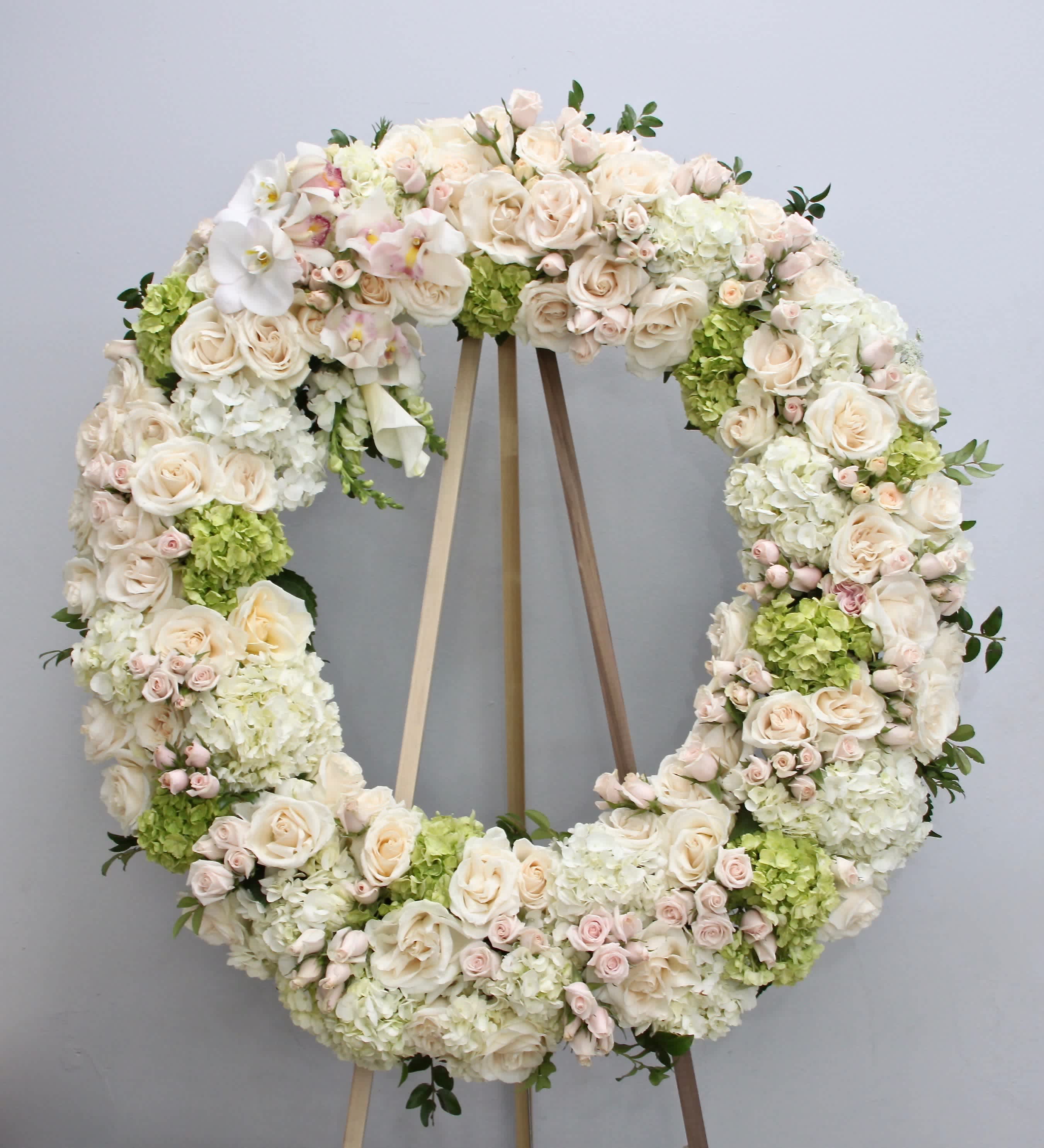 Blush Pink Wreath  - Covered in whites, greens, and pinks, this wreath is approximately 30 inches wide for standard, 36 inches wide for deluxe, and 42 inches wide for premium.      We include easel, printed banner, and delivery (some fees may apply). An additional banner can be added for $15