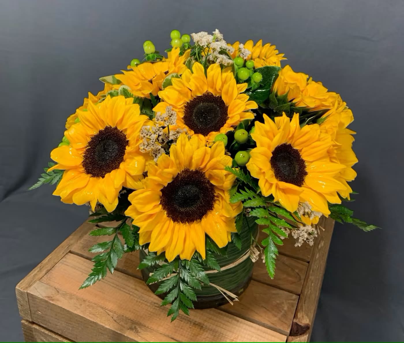 Sunflower Power - Introducing our cheerful and vibrant flower arrangement featuring ten sunflowers in a leaf-lined cylinder vase. This stunning display is a true celebration of the beauty and warmth of the sun.  The sunflower is a symbol of happiness, joy, and positivity, and each flower in this arrangement is a testament to its symbolism. Their bright yellow petals, bold and striking, create an inviting and captivating display. The sheer size of the sunflowers brings a sense of grandeur and radiance that fills any space with warmth and light.  Accented by the leaf-lined cylinder vase, this arrangement exudes a sense of natural beauty and elegance. The greenery adds texture and depth to the display, while the vase provides a contemporary and minimalist touch. The transparency of the vase allows the beauty of the sunflowers and greenery to shine through, creating a harmonious composition.  Whether it's to celebrate an important occasion, to send a message of appreciation, or simply to brighten someone's day, this arrangement is a perfect gift. It is a beautiful and elegant display that exudes positivity and happiness, inviting everyone around to bask in their warm glow.  Experience the beauty and joy of the sunflower with our magnificent flower arrangement featuring ten sunflowers in a leaf-lined cylinder vase. Let the warmth and radiance of these flowers breathe life and energy into any space, lifting spirits and brightening moods with their natural beauty.
