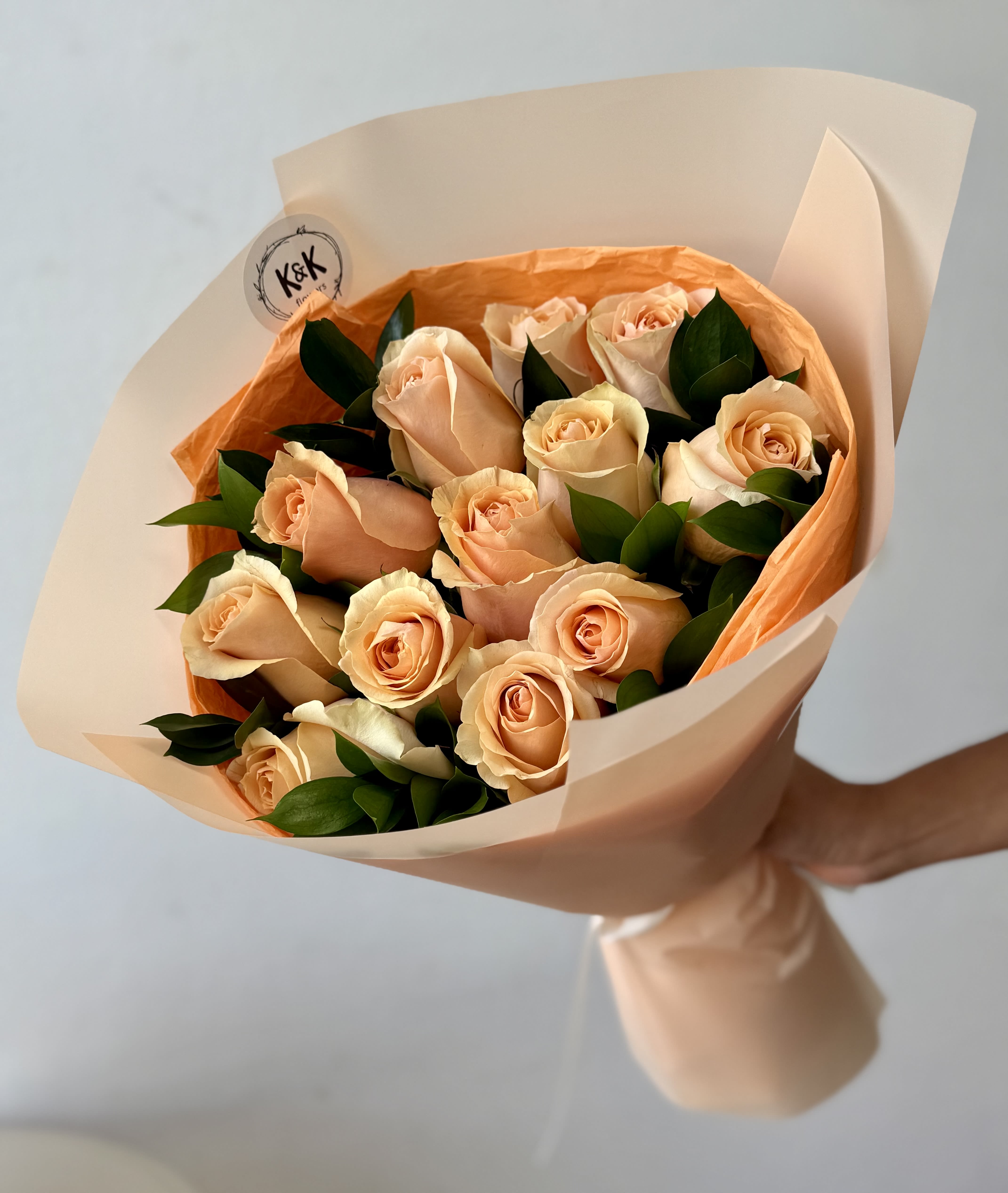 Dozen Roses Peach  - Peach Roses with greenery and decorative wrapping paper. All bouquets come without a vase; you can choose one in the add-on section.  Standard- 24 stems Deluxe- 24 stems Premium- 50 stems  Note: Flower food, transportation bag, and flower care instructions are included