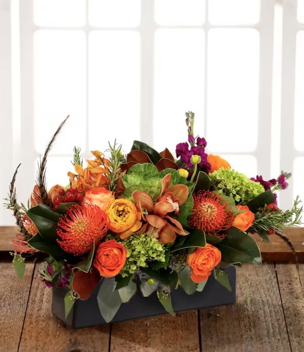 Autumn Wildfire Centerpiece - Exquisite garden table centerpiece featuring garden roses, orange protea, berry stock, garden kale or antique green hydrangea, orchid blooms, magnolia, silver eucalyptus and pheasant feathers artfully designed in a seasonal container.  Orientation: All Around.