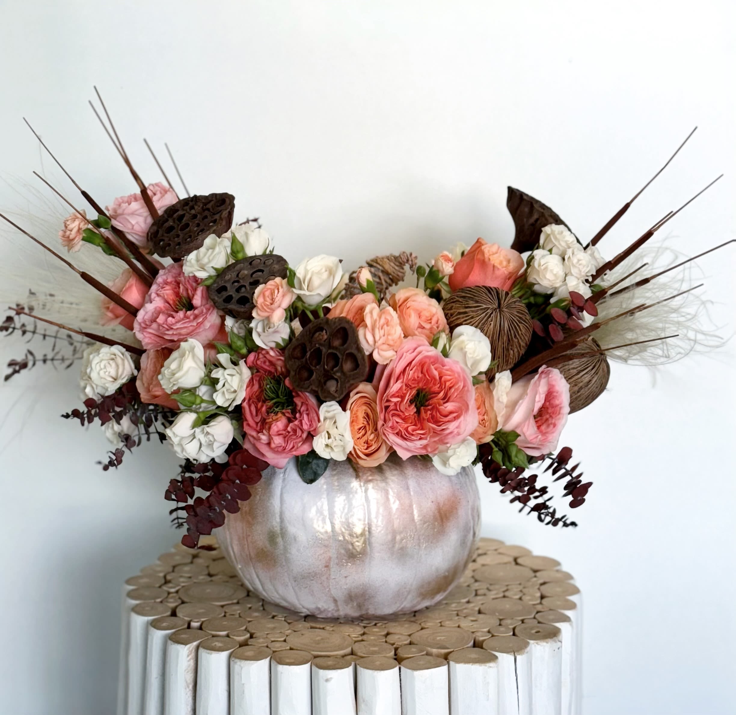 Pumpkin Whisper - A stunning autumn centerpiece arranged in a metallic pumpkin vase, filled with Roses, Spray Roses, and textured natural pods. A beautiful choice for Thanksgiving tables or cozy seasonal décor.
