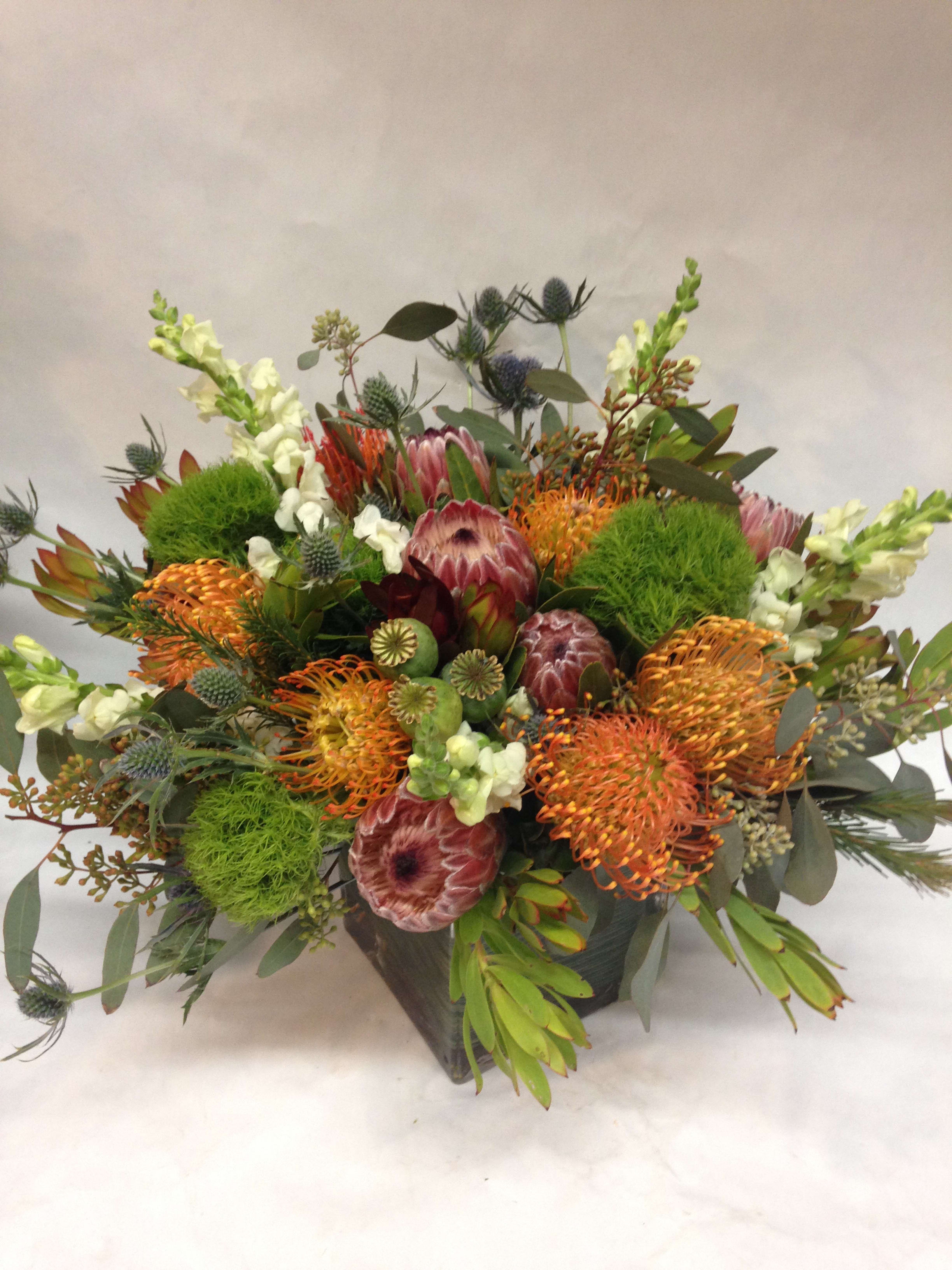 Uniquely Extravagant Arrangement  (LONG LASTING) - A quirky and stylish arrangement of long lasting flowers featuring two types of protea, dianthus, thistle, snapdragon, euacalyptus, tropical greenery, and seasonal fillers.  (Some flowers may be subject to change depending on the season. We will contact you with available flower substitutions; please contact us with specific questions if you are concerned with flower availability, thanks!)  Featured Arrangement: $178.00
