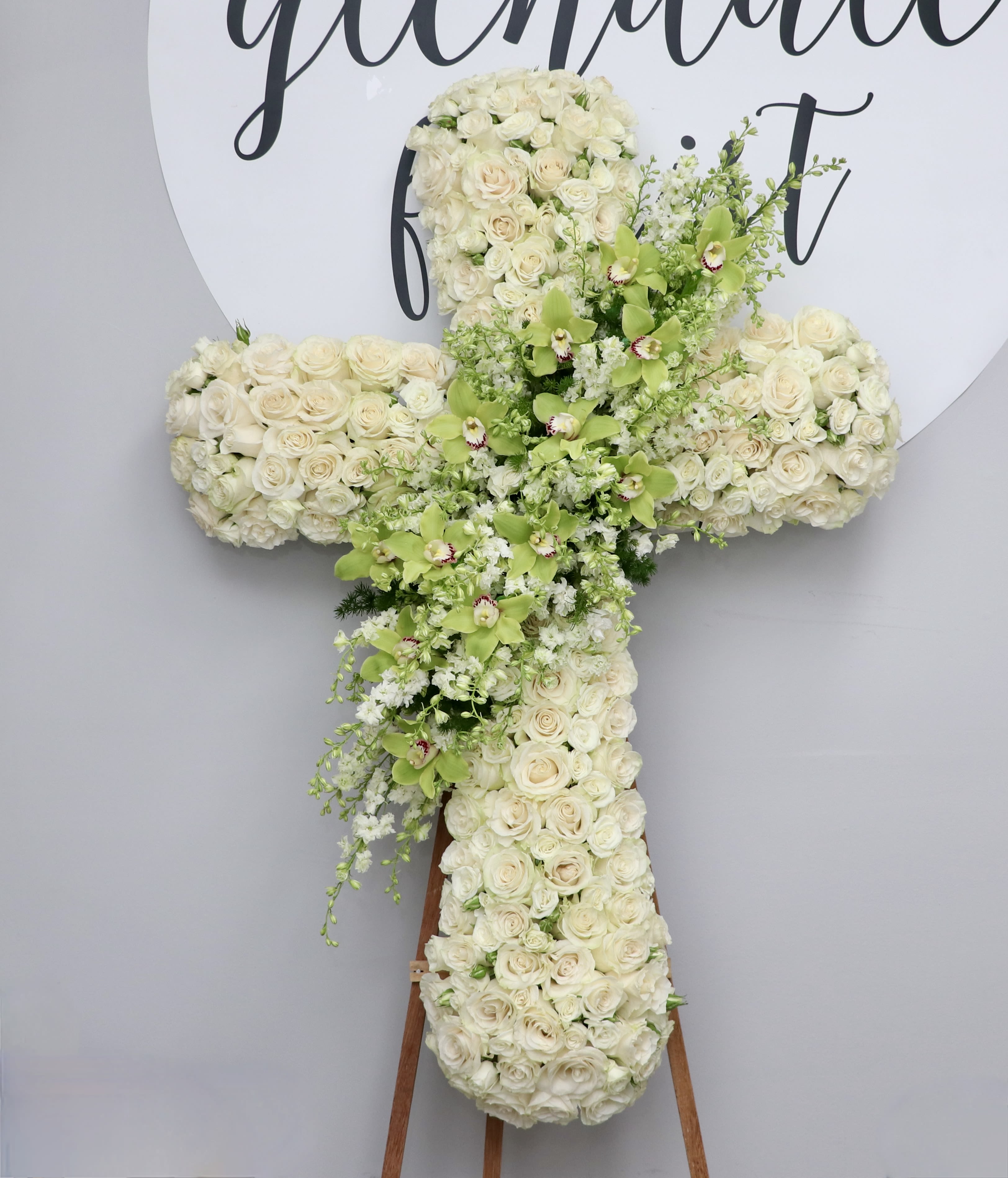 Green Orchid Remembrance Cross - This cross is made with beautiful white roses with an extravagant display of green cymbidium orchids in the center. A gorgeous choice to honor your loved one.  We include easel, printed banner, and delivery (some fees may apply). An additional banner can be added for $15.  Standard size is 30'', deluxe is 36'', and premium is 42''. 