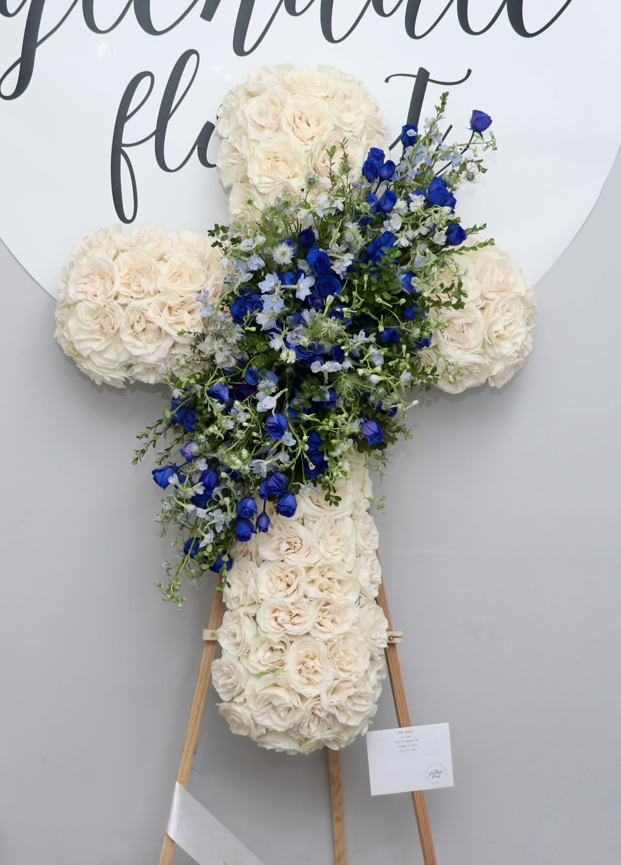 Soothing Skies  - This sympathy cross is made with white roses and accented with a blue design in the center.    We include easel, printed banner and delivery (some fees may apply). An additional banner can be added for $15.  Standard size is 30'', deluxe is 36'', and premium is 42''.