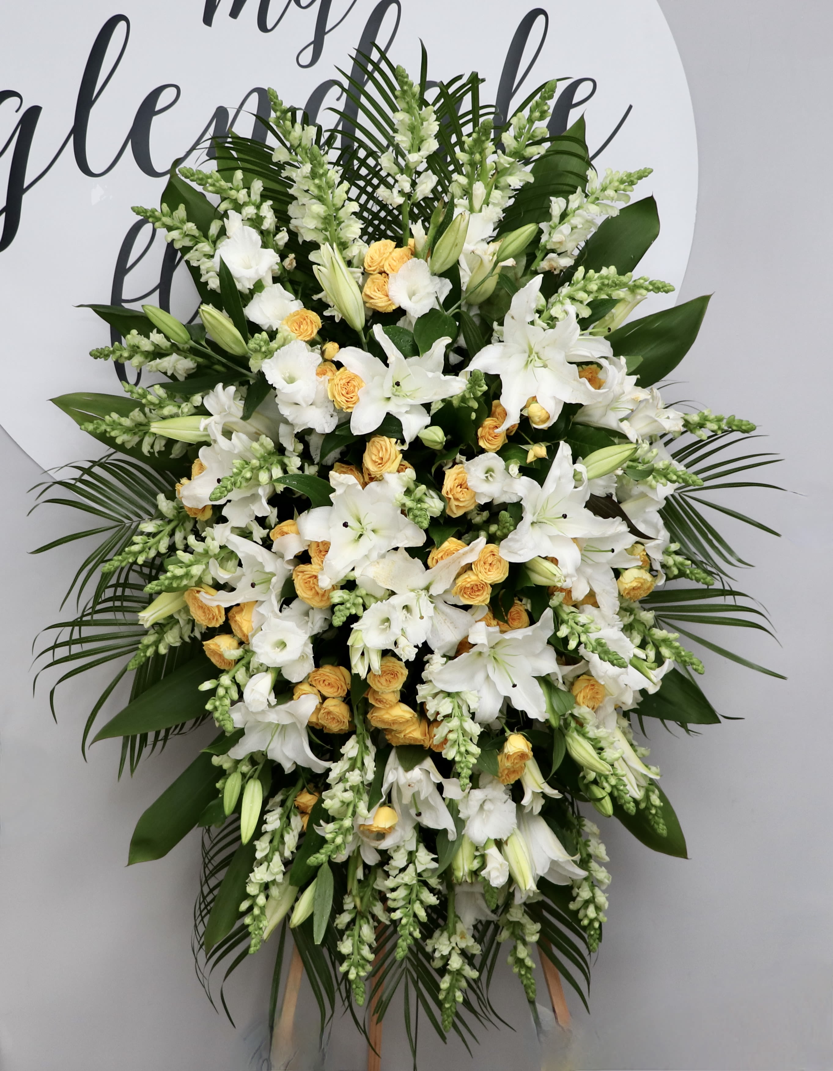 Sunshine Spray  - This sympathy spray includes bright yellow roses, stargazer lilies, and seasonal greens.     We include easel, printed banner and delivery (some fees may apply). An additional banner can be added for $15.    Standard size is 30'' wide, deluxe is 36'', and premium is 42''.