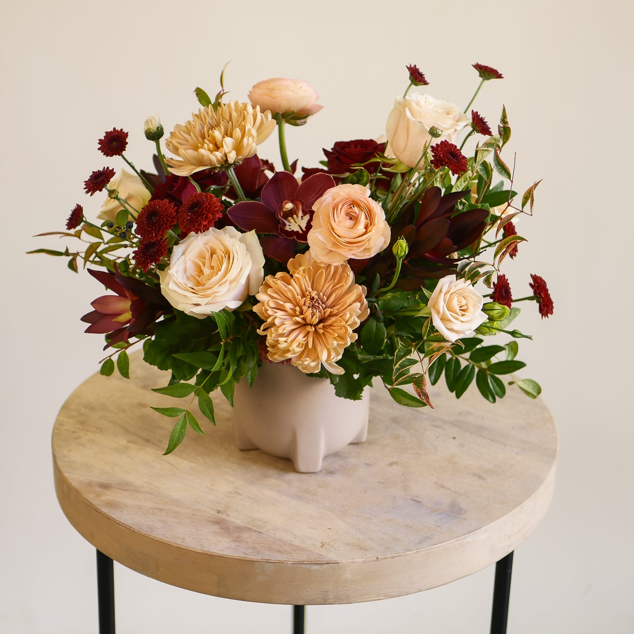 Merlot Kiss - Merlot Kiss captures the essence of cozy holiday gatherings with a rich palette of warm peach, deep burgundy, and golden tones. Featuring garden roses, chrysanthemums, ranunculus, cymbidium orchids, and lush seasonal greenery, this elegant arrangement bridges the beauty of autumn and the magic of winter. Designed in a modern blush-toned ceramic vase, it’s the perfect centerpiece for holiday tables, festive celebrations, or as a thoughtful gift for loved ones. Bring warmth, texture, and timeless sophistication to your home this season with a piece that embodies LA’s modern holiday style.  Handcrafted by our designers in West Los Angeles, Merlot Kiss is available for same-day delivery (before 1pm) across Santa Monica, Beverly Hills, Brentwood, Westwood, Pacific Palisades, and surrounding areas.