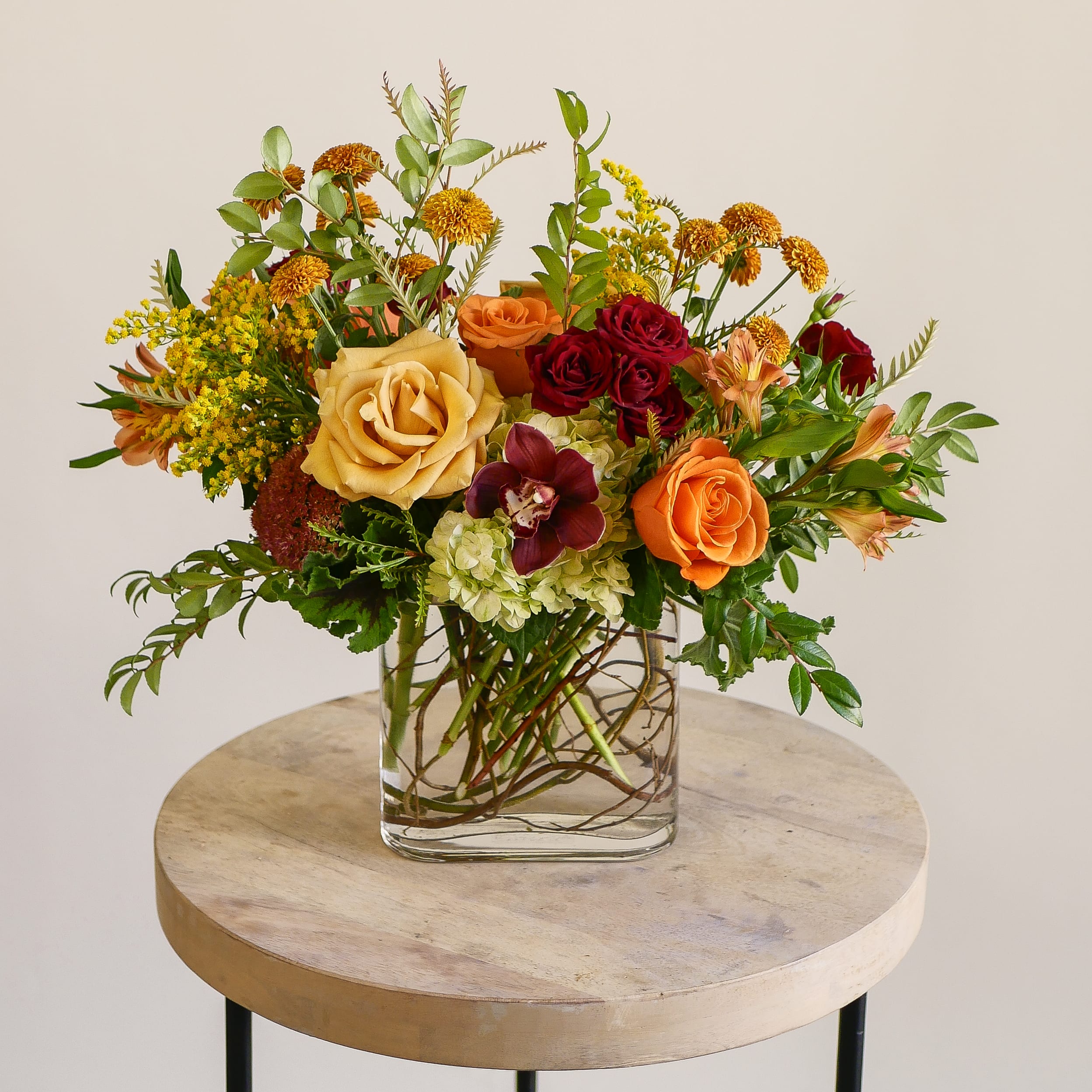 Fall Radiance - Bring the beauty of the season indoors with Fall Radiance — a warm and vibrant fall arrangement that captures the essence of a California autumn. Featuring golden and orange roses, burgundy cymbidium orchids, deep red spray roses, hydrangea, and bronze accents, this design glows with natural elegance. Arranged in a modern clear glass vase with artistic curly willow branch details, Fall Radiance is ideal for Thanksgiving centerpieces, fall celebrations, or as a seasonal gift for someone special.  Expertly crafted by our floral designers in West Los Angeles, this autumn arrangement is available for same-day delivery throughout Santa Monica, Brentwood, Beverly Hills, Westwood, Pacific Palisades, and nearby areas.