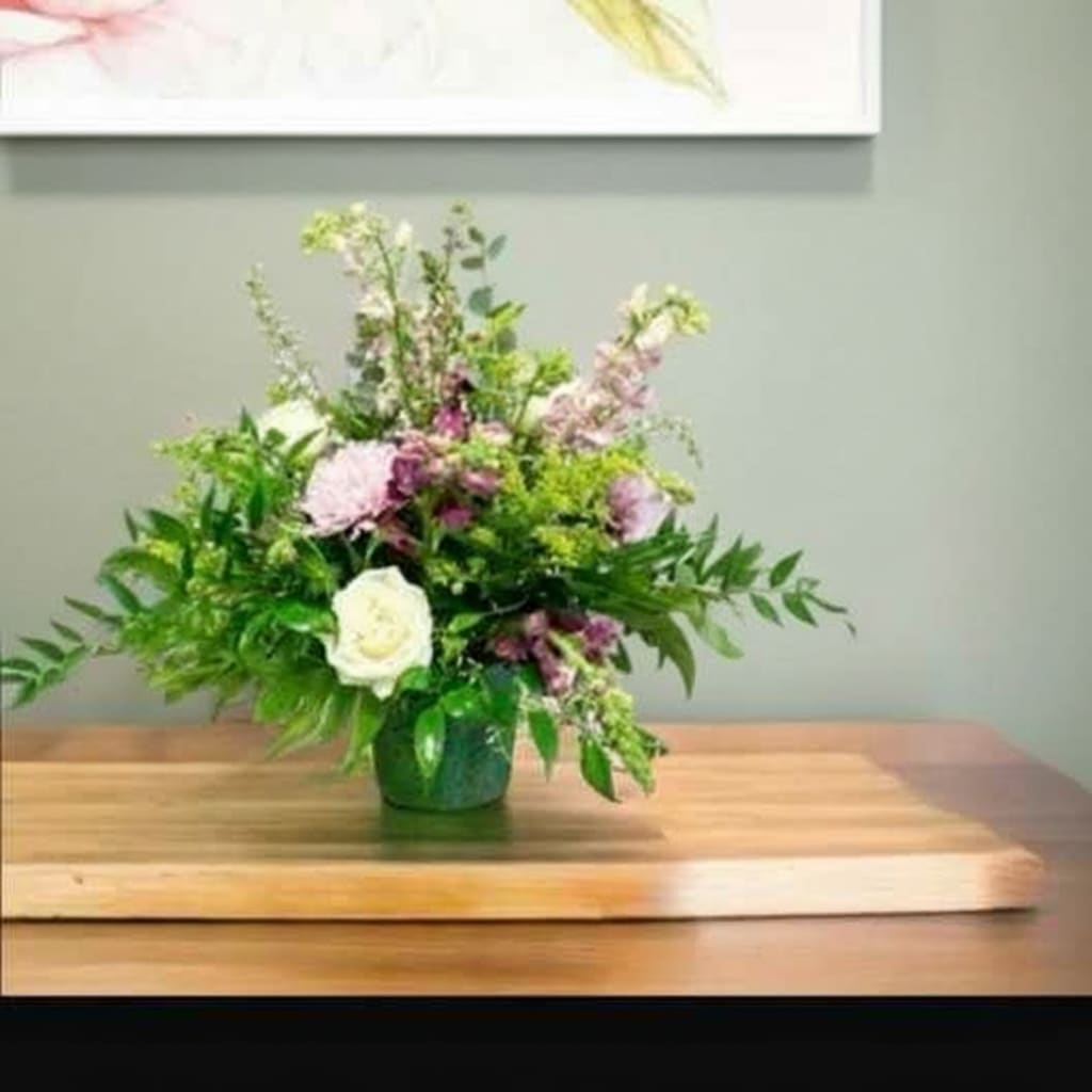 Strength and Silence  - Soft, graceful, and quietly powerful—Strength and Silence speaks volumes through its gentle beauty. Featuring serene tones of ivory, lavender, and fresh greens, this arrangement includes elegant roses, mums, snapdragons, solidago, and lush greenery thoughtfully arranged in a traditional mache basket.  Perfect for offering comfort during times of loss or quiet reflection, this piece conveys strength, peace, and heartfelt sympathy with every stem.