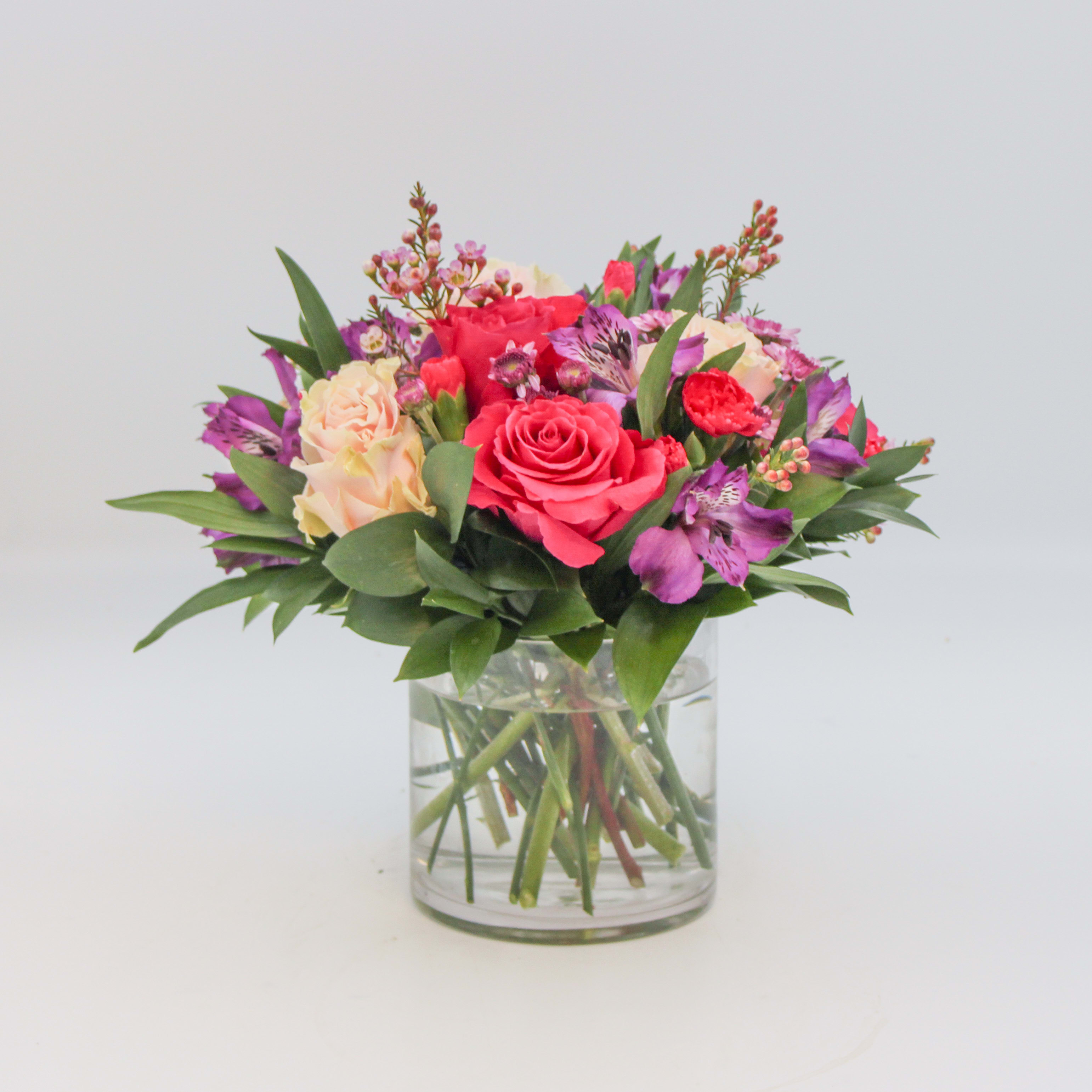 Vanessa - Vanessa is a colorful assortment of Purple Alstroemeria, Hot Pink Roses, Light Pink Roses, Lavender Button Mums, Pink Waxflower and Israeli Ruscus arranged in a clear glass cylinder. The Standard size Vanessa is arranged in a 5 inch cylinder and the Deluxe sized Vanessa is arranged in a 6 inch cylinder.