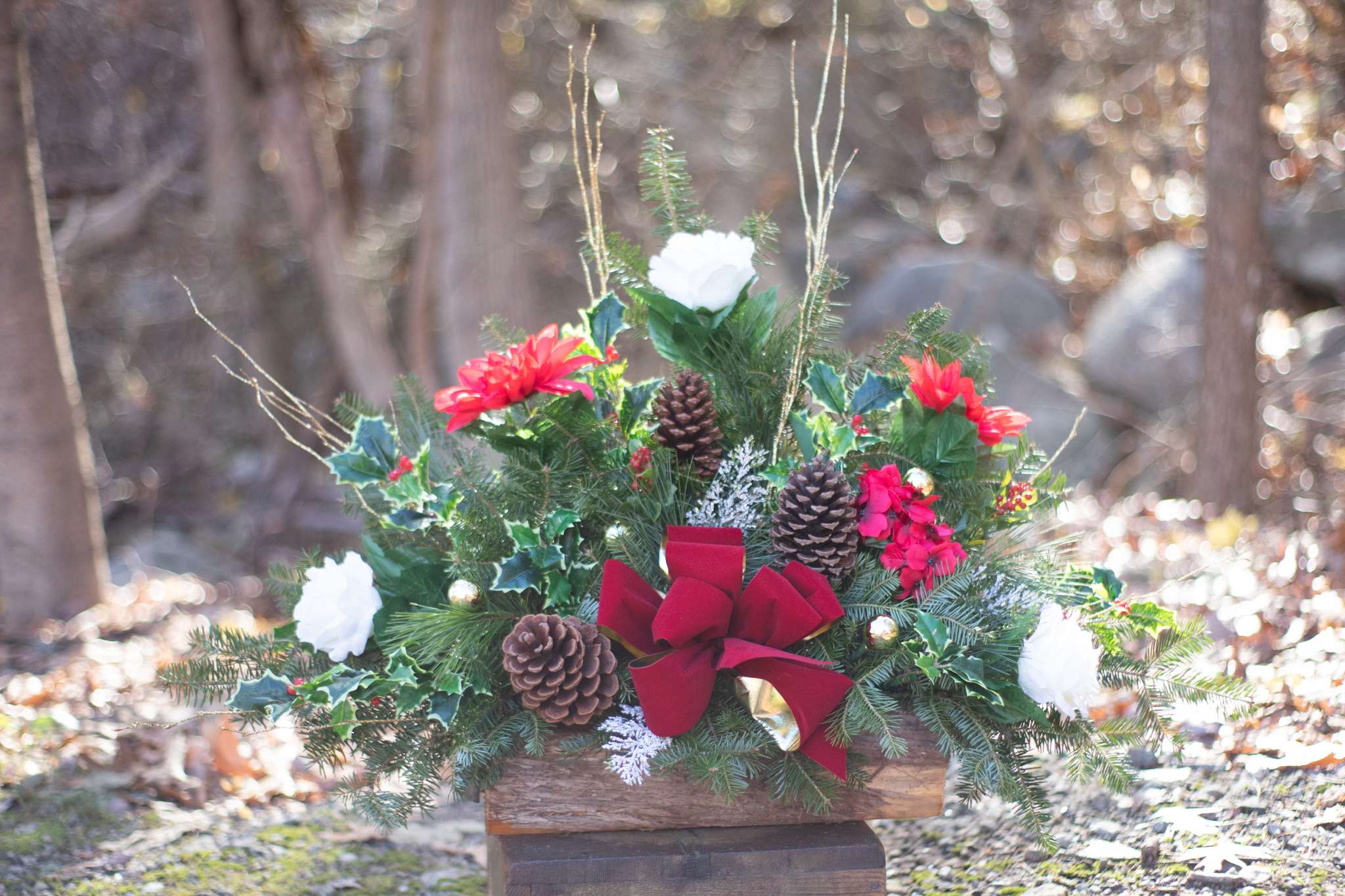 Cemetery Winter Arrangement Deluxe - A special arrangement in memory of your loved one. These arrangements are designed to sit on the ground in front of family monuments. This size includes a longer wood box with a traditional upright design. Fresh winter foliage with artificial décor to last through the winter season. Boxes do vary in size as they are handcrafted from natural materials. They generally do not exceed 15 inches in length. Upgrading will allow us to add additional decorative items to the design. All designs are one sided as the back faces the stone monument.