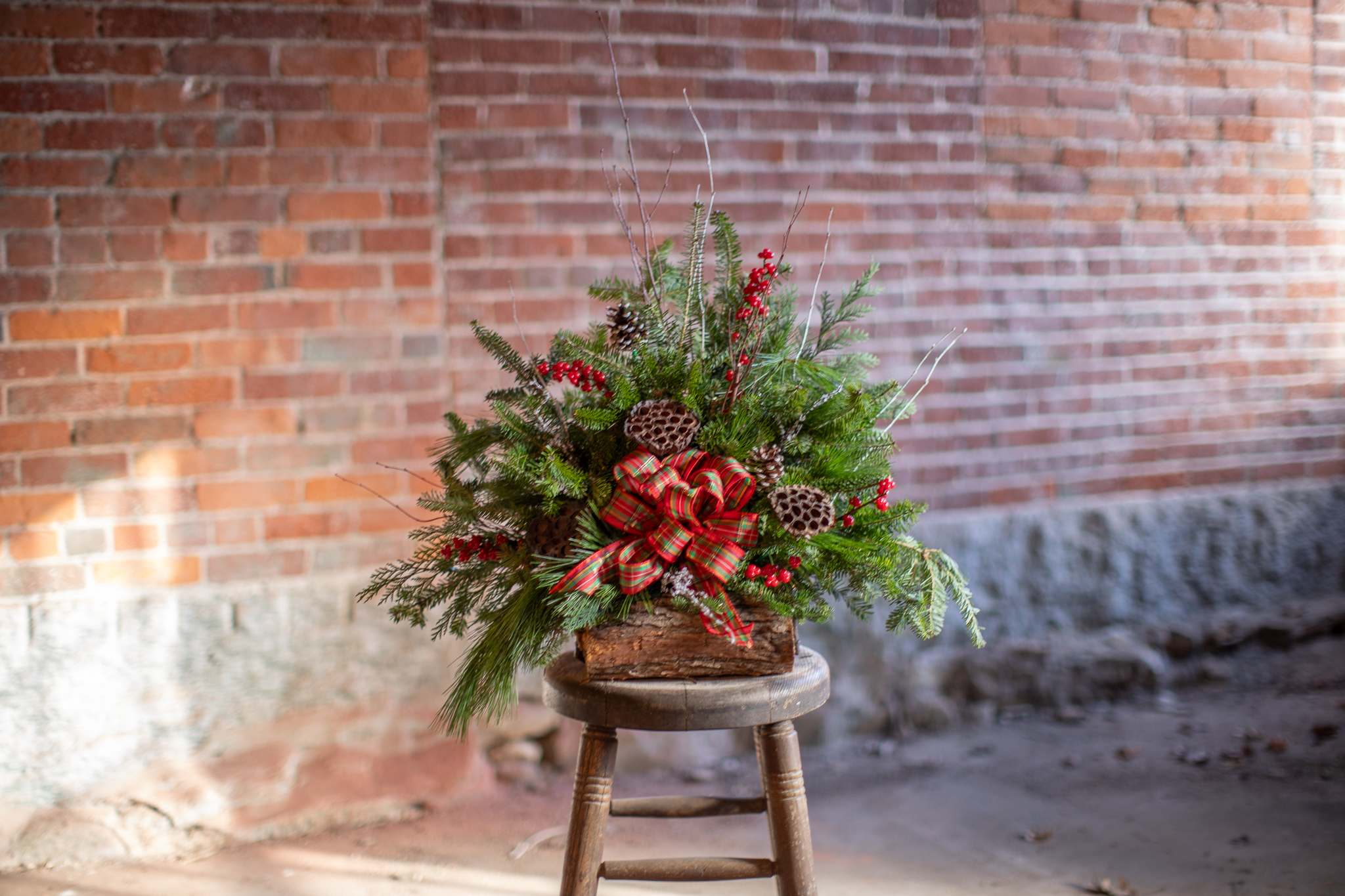 Cemetery Winter Arrangement Standard - A special arrangement in memory of your loved one. These arrangements are designed to sit on the ground in front of family monuments. Standard size includes either a medium wood log box with a taller upright design or a longer wood box with a low design. Fresh winter foliage with artificial décor to last through the winter season. Boxes do vary in size as they are handcrafted from natural materials. They generally do not exceed 15 inches in length. Please specify if you'd like a long and low design or a taller upright traditional design. If not provided in the special instructions we will create something lovely. Upgrading to deluxe will allow us to add additional decorative items to the design. All designs are one sided as the back faces the stone monument.