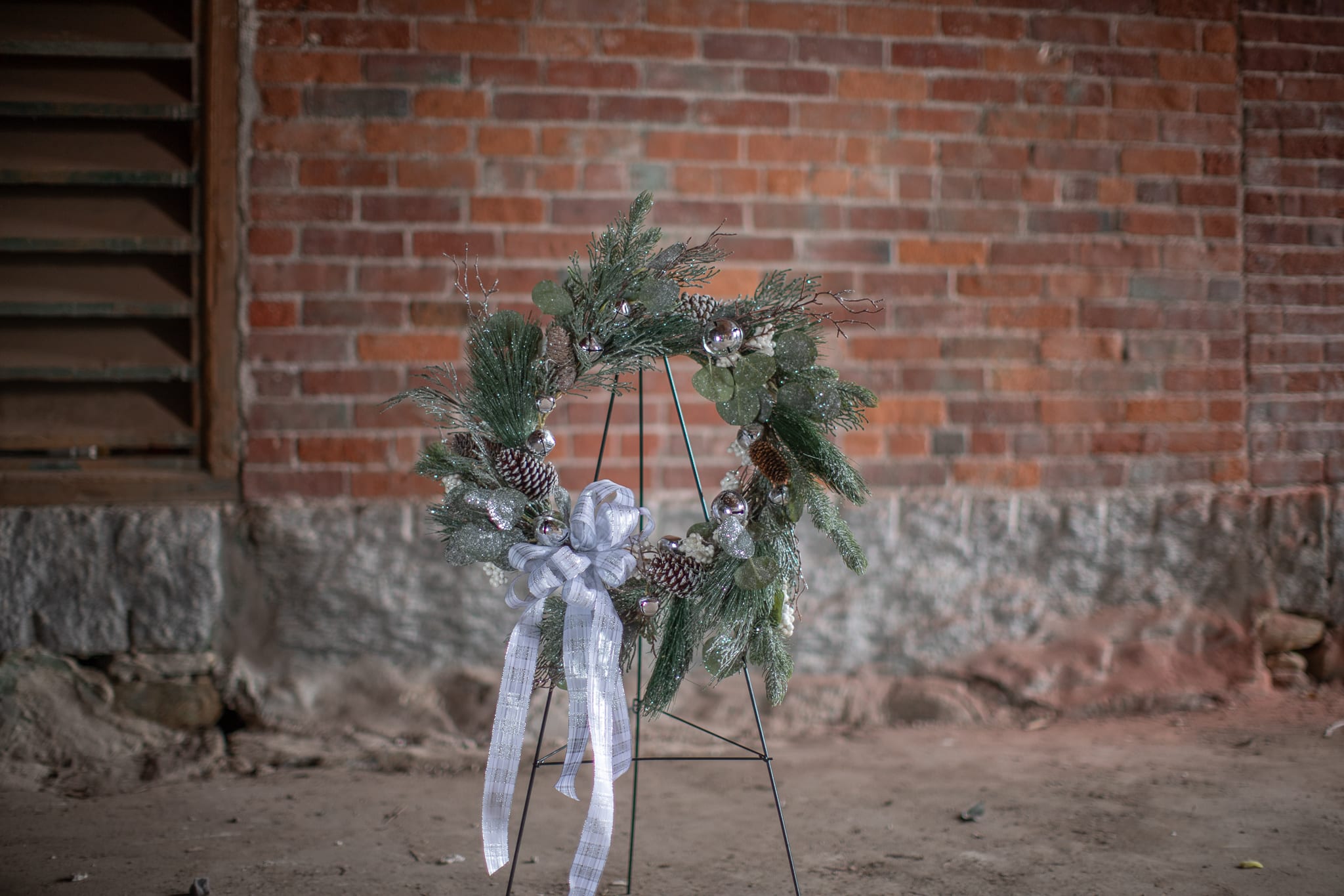 SALE! Silver Jingle Bells Wreath (Artificial) - Twinkling glittery winter foliage of pines, silver dollar eucalyptus, and spruce varieties decorated with white tip pine cones, white berries and silver bells. Perfect to deck the halls. A white and silver plaid bow complete this beautiful wreath. 22 inch overall diameter. Upgrade to premium pricing for a pair. Permanent floral decor is the gift that keeps on giving year after year. 
