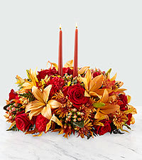 Bright Autumn Centerpiece  - Fall is all about coming together and making memories with one another. The Bright Autumn Centerpiece helps make those precious moments even more special. With red roses, peach Asiatic lilies and red carnations and bronze cushion poms embracing 2 taper candles, this centerpiece is a beautiful gift for every Autumn occasion.