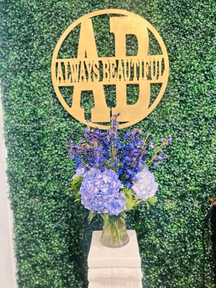 Delphinium &amp; Hydrangea - This striking floral arrangement features a harmonious blend of soft blue hydrangeas and deep purple delphiniums. The rich blue hues create a stunning contrast, while the fresh greenery adds a touch of vibrancy and texture. Arranged in a simple glass vase, this piece exudes elegance and sophistication, making it perfect for any setting that calls for a pop of color.  Ideal for adding a calming and regal touch to any room, this arrangement is perfect for celebrations, weddings, or as a beautiful gift for someone special. The cool blue and purple tones create a serene and graceful atmosphere.