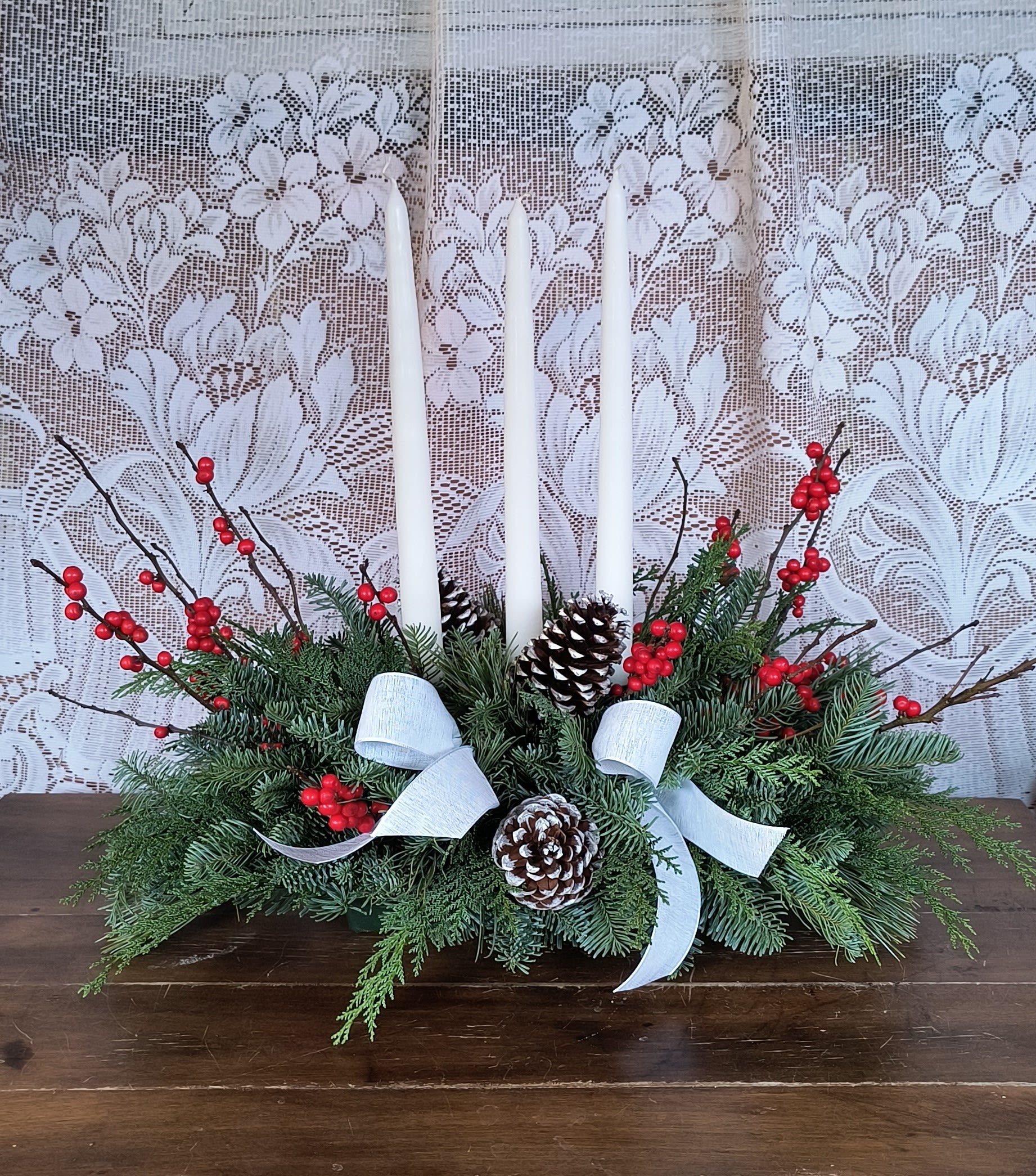 Blessings - Feel the blessings all around you this holiday season. Celebrate with this simple elongated evergreen centerpiece with fresh winterberries and snow white candles and ribbon. approx. 20&quot; W