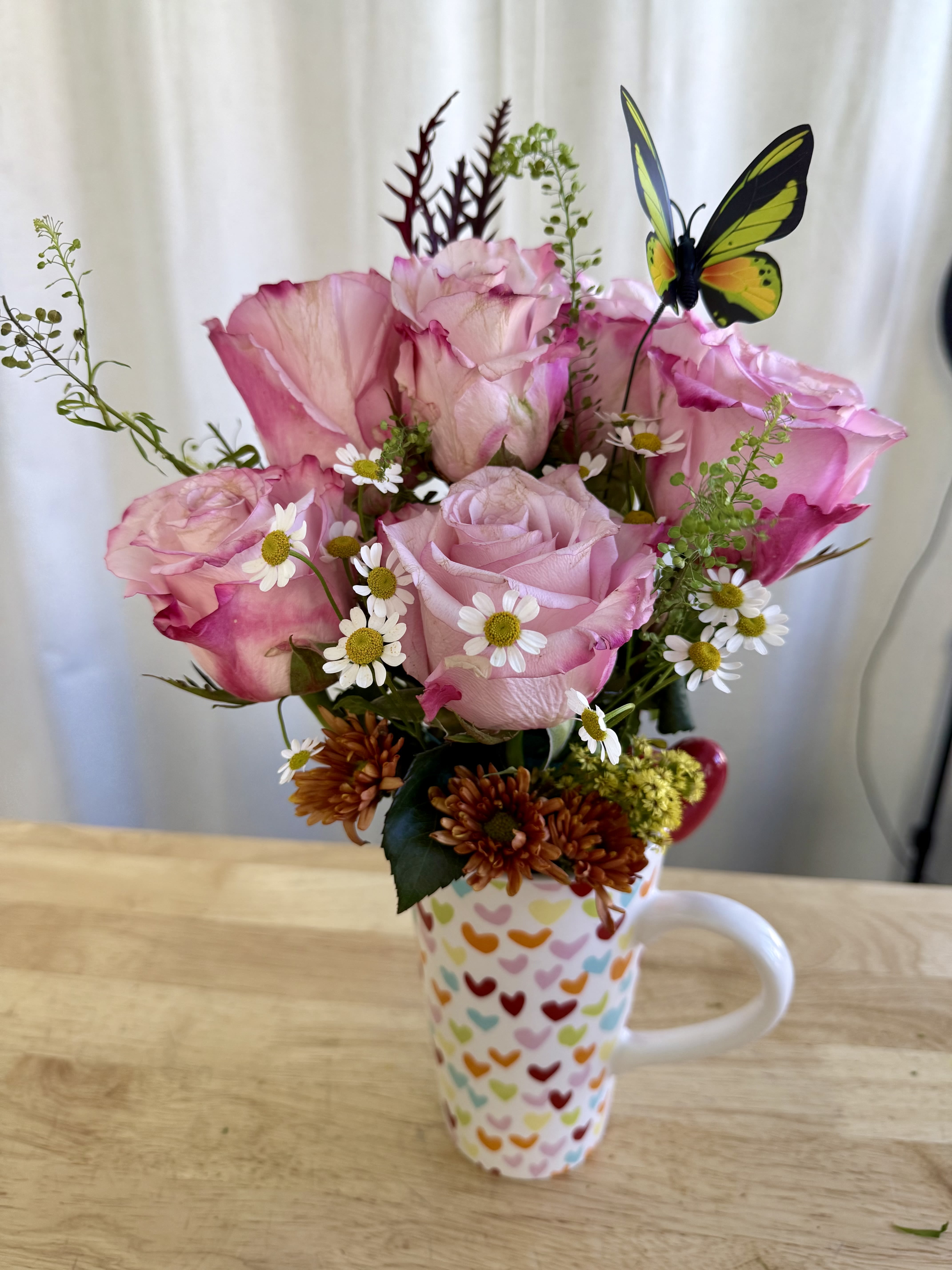 Cup of hearts - A delicate arrangement featuring soft pink roses, daisies, and wildflower accents in a heart-patterned mug. A charming touch of color and tenderness — perfect for brightening someone’s day or gifting with love.