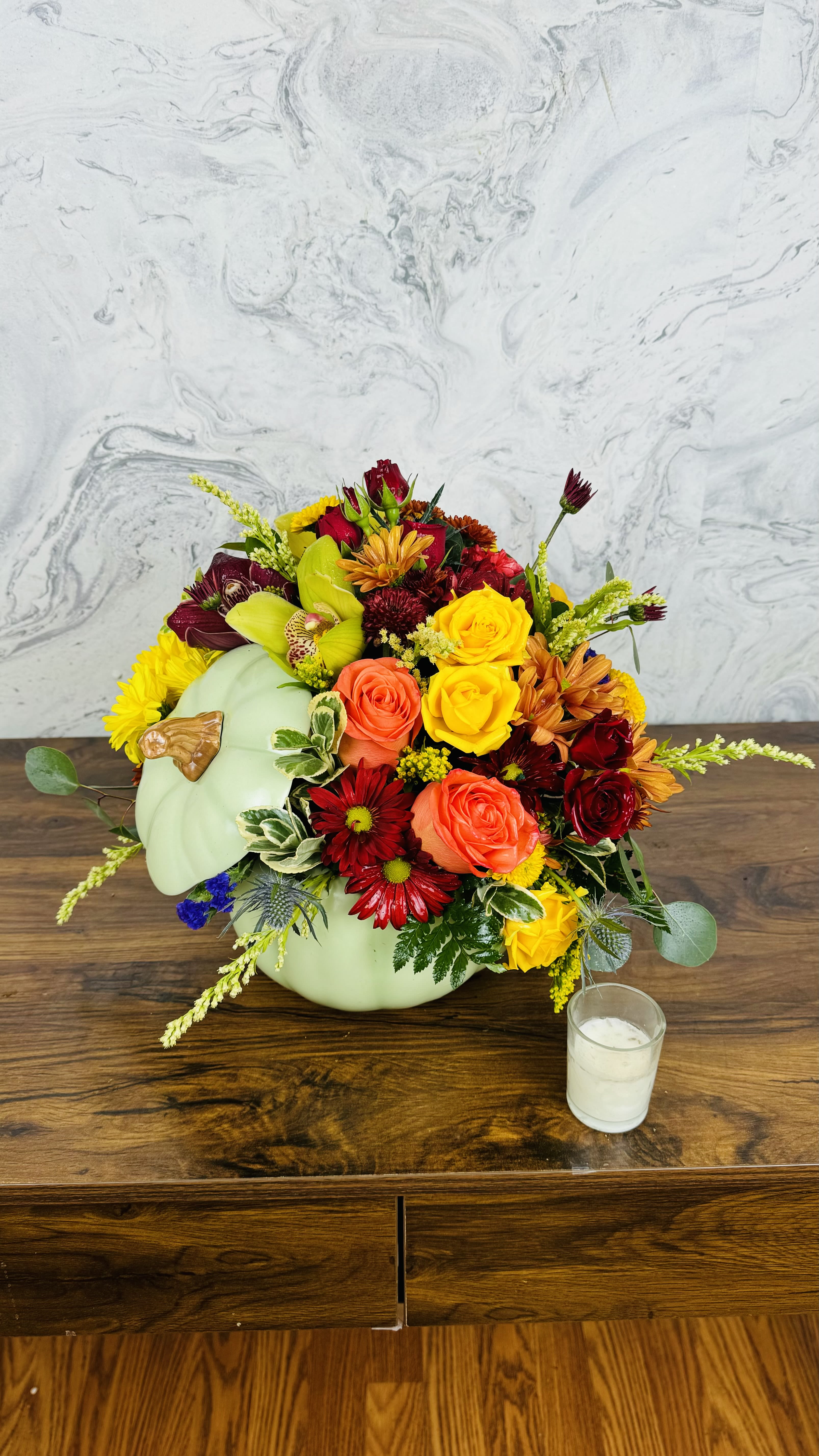 Autumn pumpkin Elegance - This stunning arrangement captures the essence of fall with a delightful mix of vibrant flowers. Nestled in charming ceramic pumpkin containers, the arrangement features elegant cymbidium orchids, known for their rich, lush petals, alongside soft, romantic roses. The warm hues of deep oranges, burgundies, and golden yellows evoke the beauty of autumn leaves, creating a cozy and inviting atmosphere. Perfect for seasonal decor, this arrangement brings a touch of nature's elegance to any space, celebrating the beauty of the harvest season. 