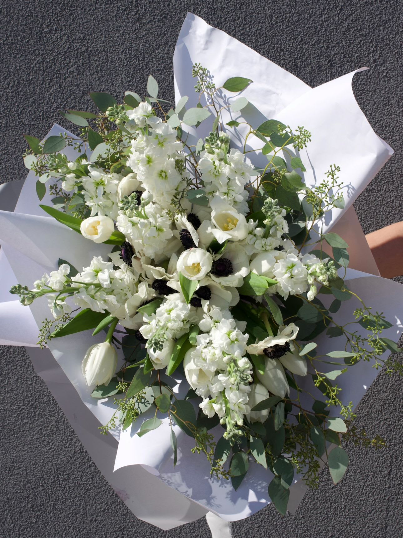 Chanel Blanc - A symphony of white and shadow, this bouquet evokes the quiet drama of a black-and-white photograph. Pure ivory blossoms, touched by velvety midnight centers, create a sophisticated balance between softness and strength. Designed for those who appreciate understated luxury, it’s a gift that lingers in memory like a timeless work of art.