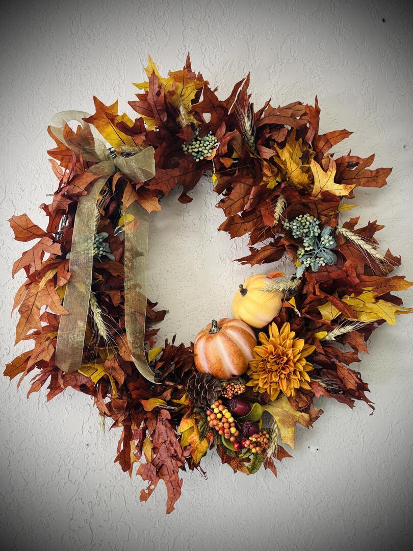 Golden Harvest Wreath - Celebrate the beauty of the season with our Golden Harvest Wreath. Handcrafted with genuine dried oak leaves and accented with lifelike pumpkins, berries, pinecones, and autumn blooms, this wreath captures the cozy spirit of fall in every detail. A soft sage colored ribbon adds a touch of rustic elegance, making it perfect for your front door, entryway, or seasonal décor.  Each piece is unique, designed to bring lasting warmth and charm to your home throughout the harvest season. 18&quot; Grapevine wreath 