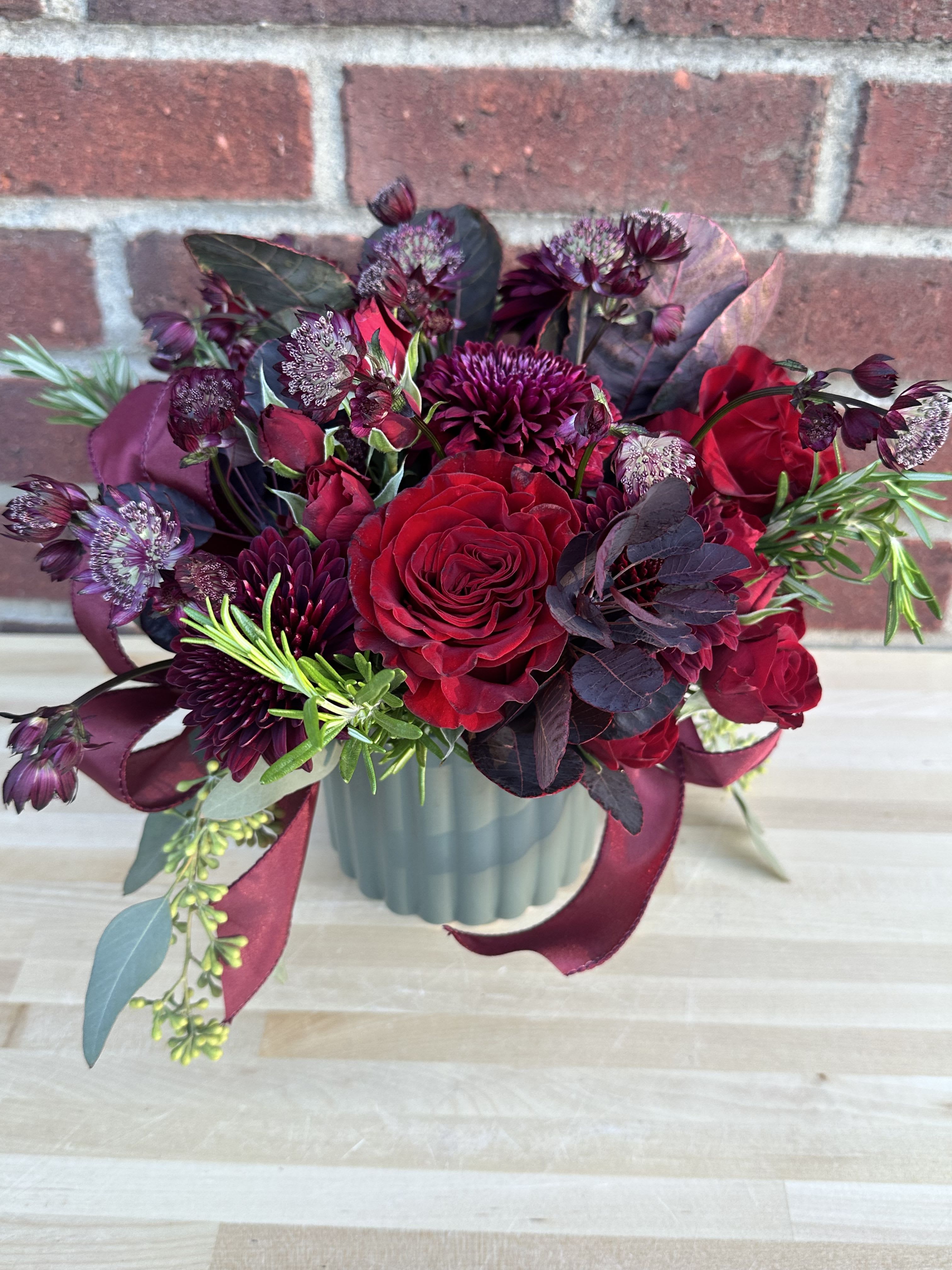 Plum Eve - A beautiful deep, rich and velvety color palate of plum and burgundy with accents of sage greens.  Including roses, spray roses, mums, astrantia, rosemary etc with specialty taffeta ribbon and a gorgeous keepsake container. 