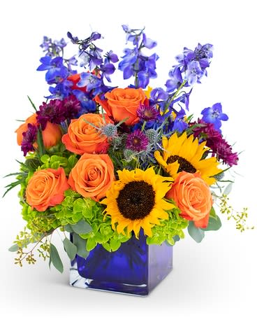 Seasonal Lights - This spectacular, brilliantly and professionally hand-designed flower bouquet, Seasonal Lights, features exotic-looking delphinium, magical roses, playful hydrangea, spray mums, and the sunshine’s warmth of sunflowers in a blue cube vase. Seasonal Lights is a flower arrangement that fills a room with excellence during the fall time, summer season, and spring days. It is a perfect gift of flowers to have delivered to the special someone on their birthday or anniversary. 